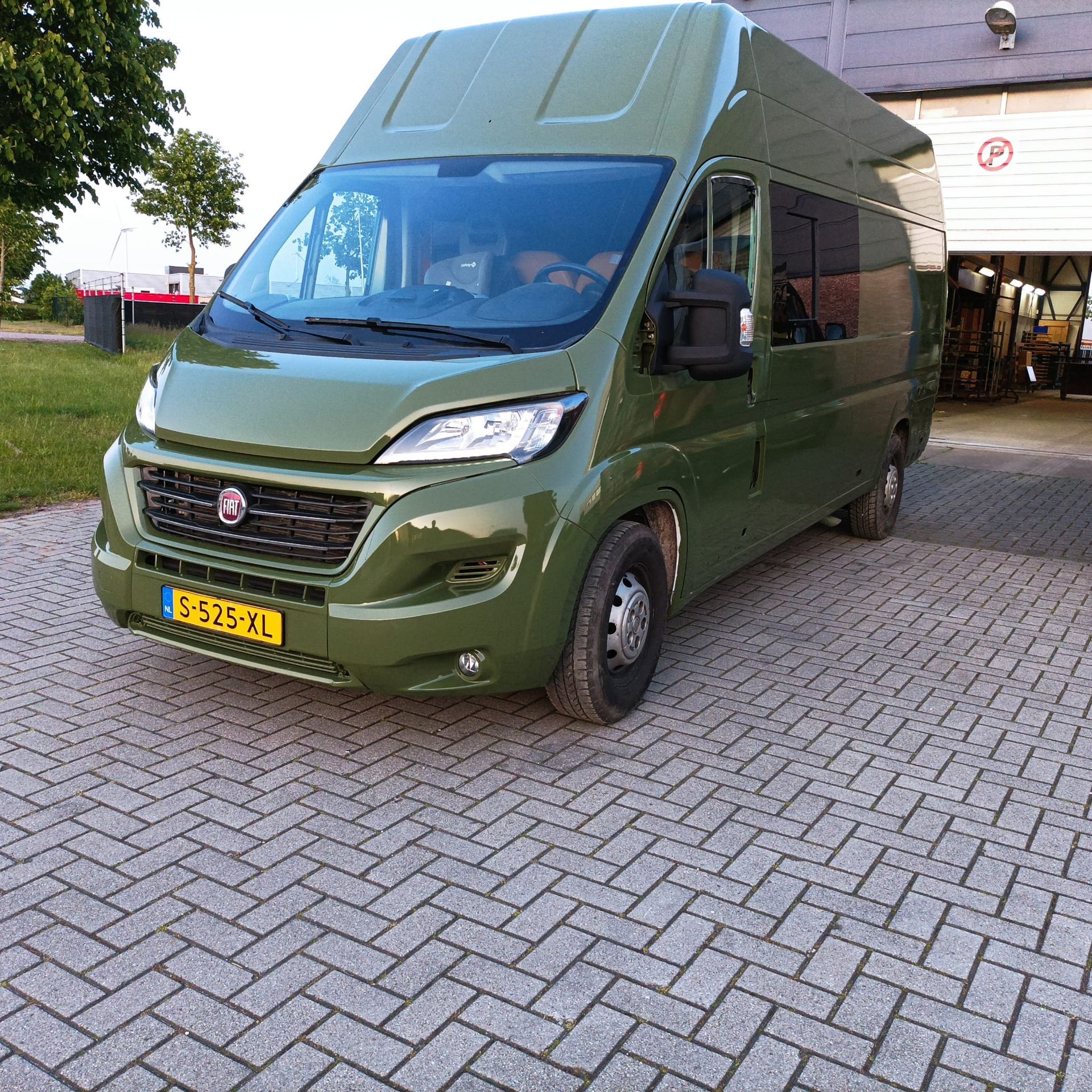 Groene camper geparkeerd op een terras van bakstenen.