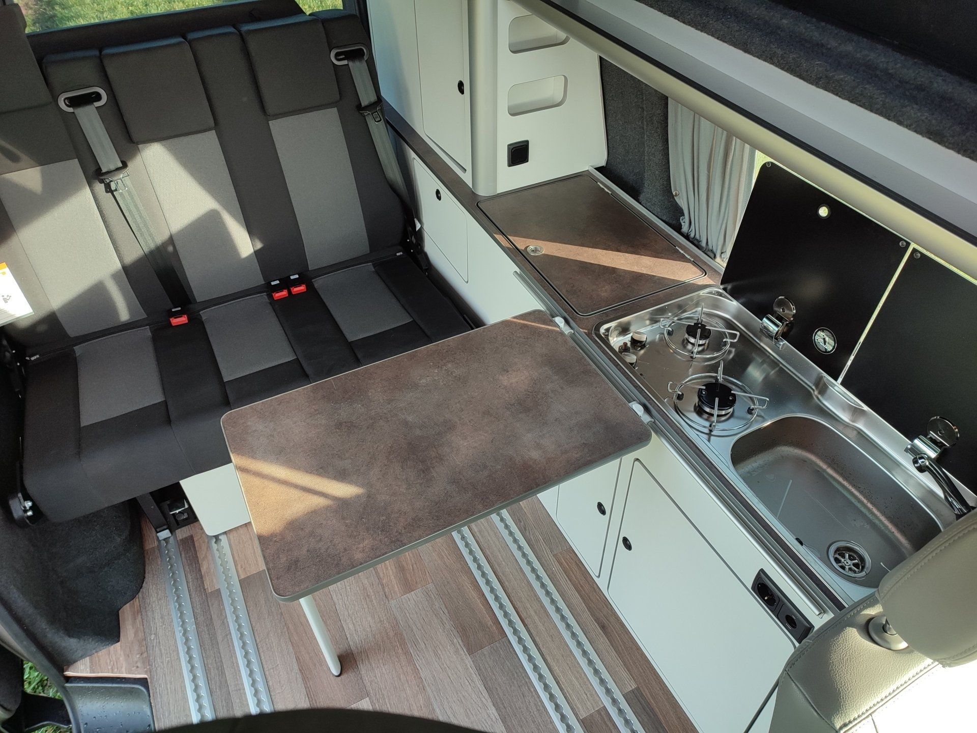 Interieur van een camper met zitplaatsen, een keukenblad met een spoelbak en een tafel.