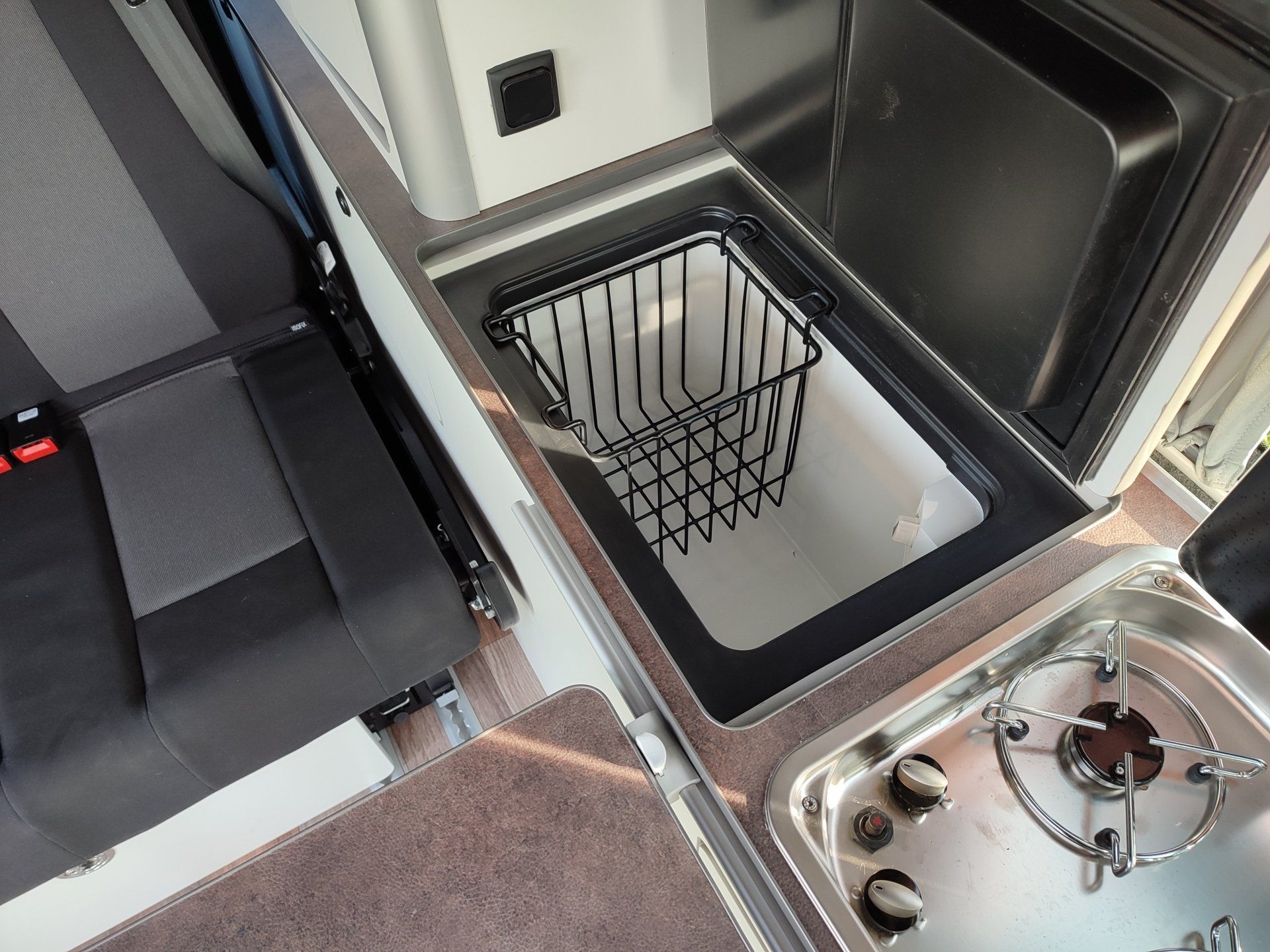 Interieur van een camper, met een kleine koelkast met een draadmand en een kookplaat.
