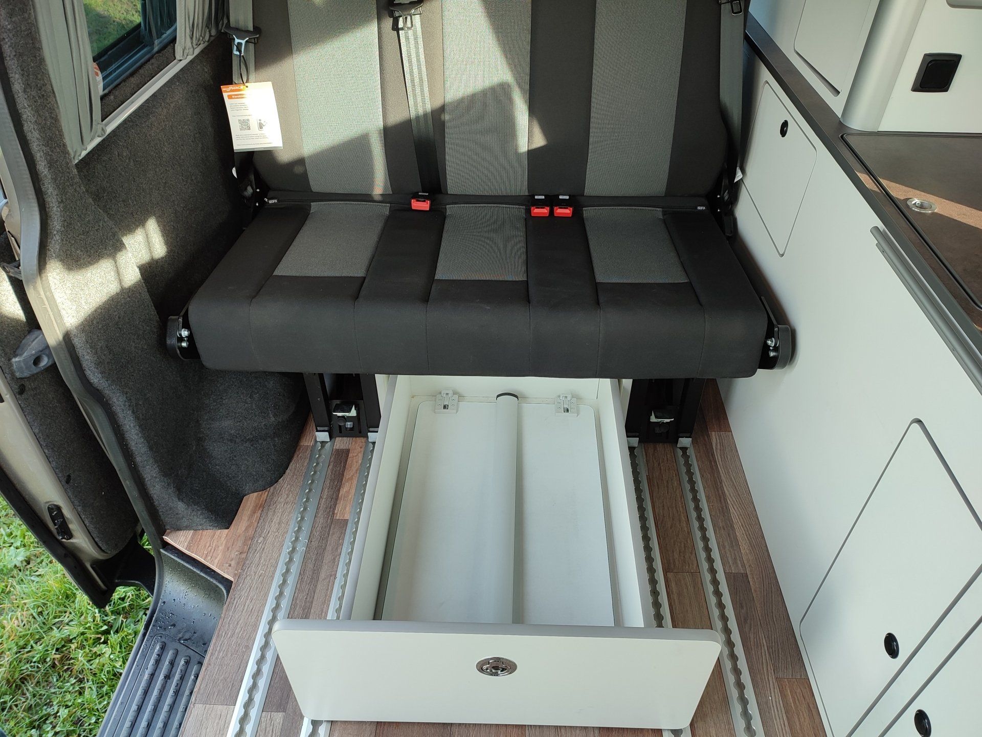 Interieur van een bestelwagen met een uittrekbare lade onder een zwart-grijze bank.