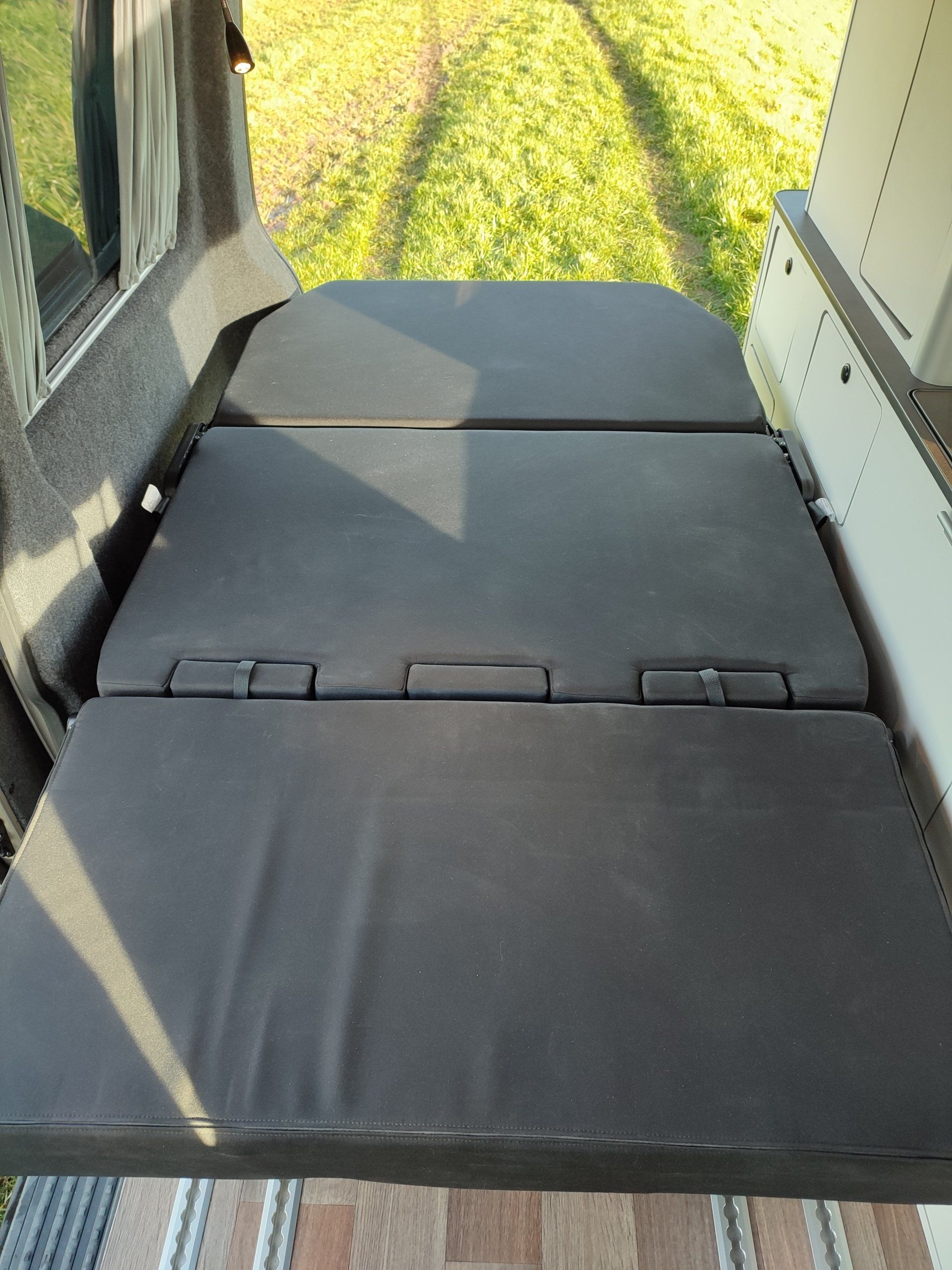 Opvouwbaar zwart matras dat vanuit een bestelwagen uitsteekt richting het groene gras.