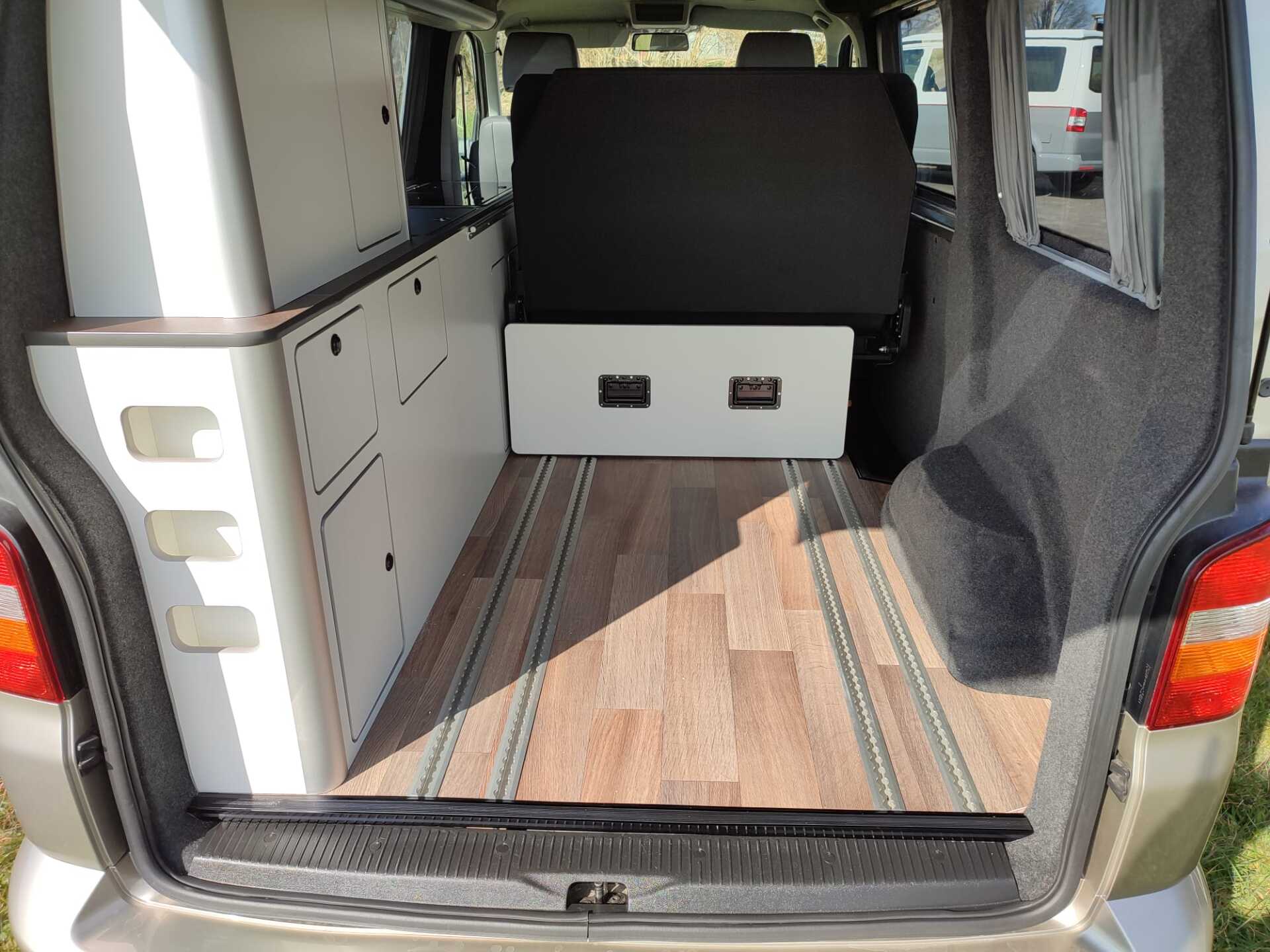 Interieur van de camper: houten vloer, witte kastjes, neerklapbare bank.