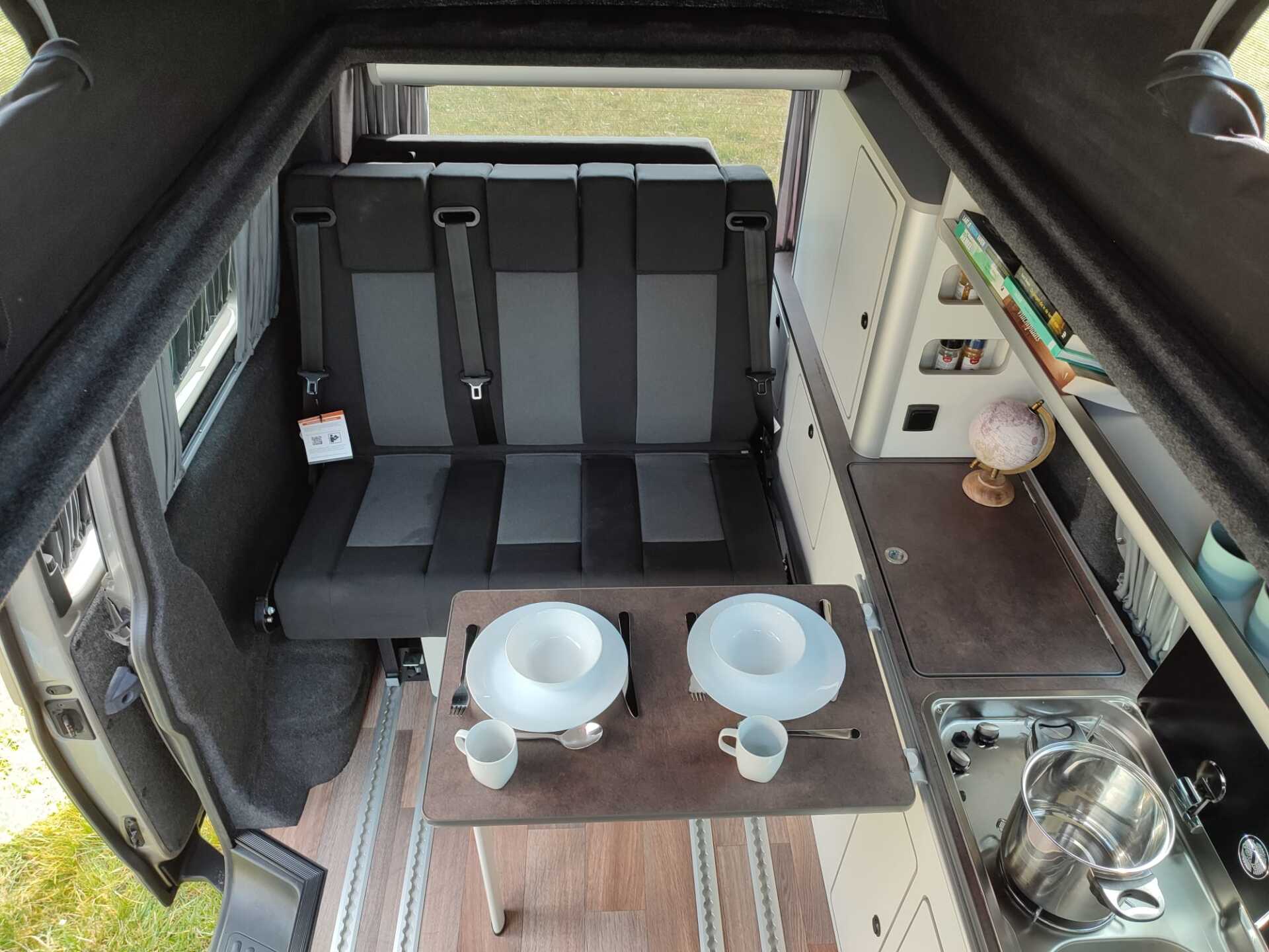 Interieurfoto van een camper met een inklapbare tafel, gedekt voor de maaltijd. Keuken en zitgelegenheid zichtbaar.