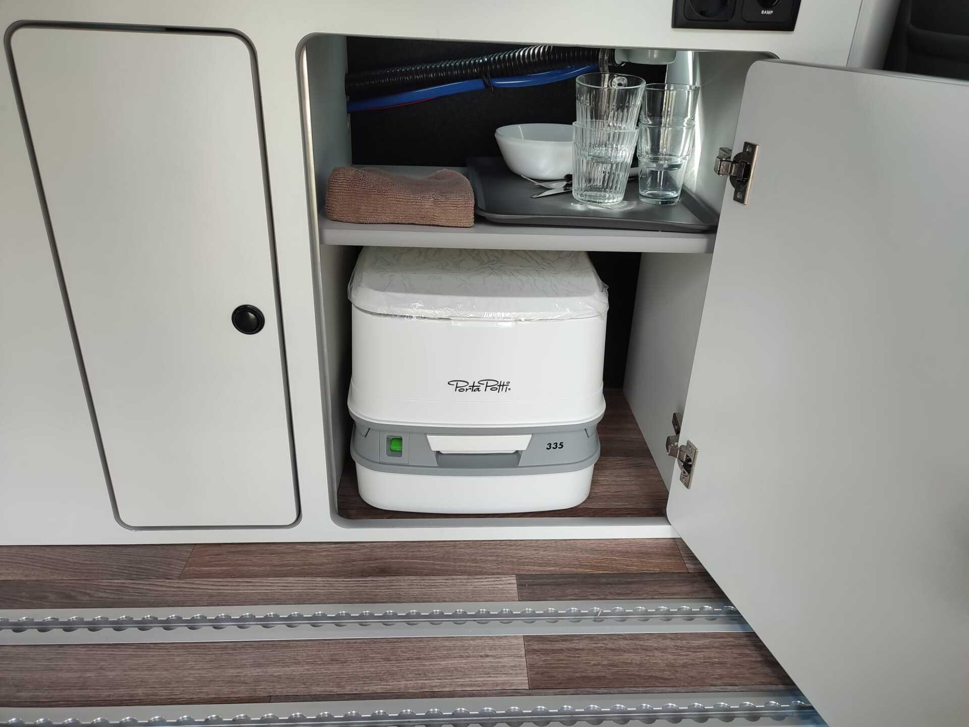 Wit, draagbaar toilet opgeborgen in een kast in een camper.