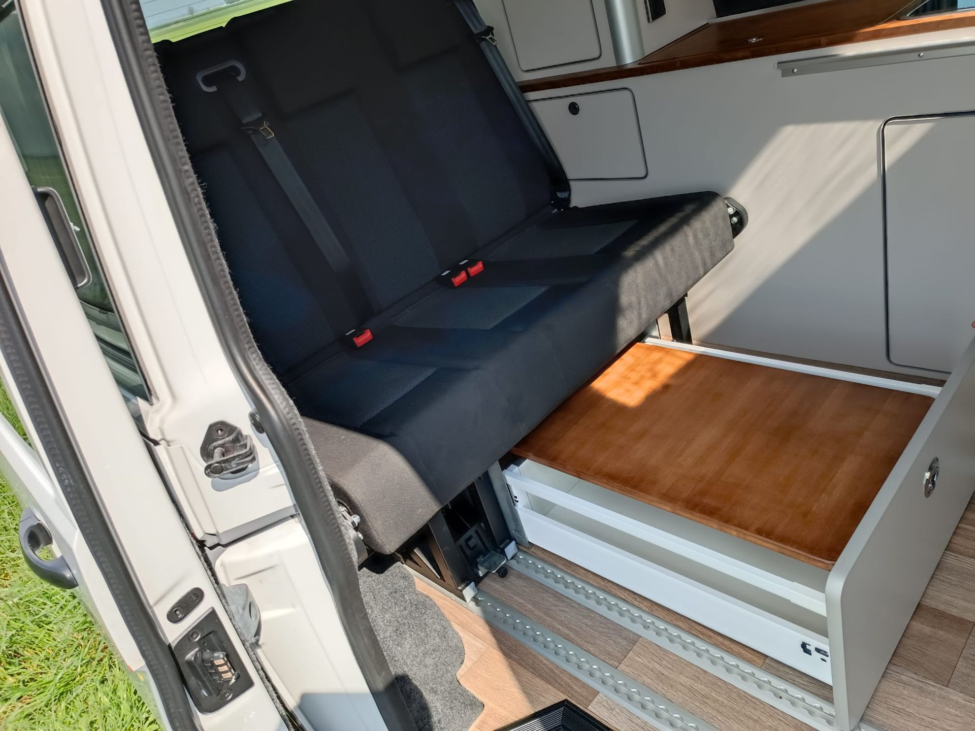 In een camper zijn een opklapbare bank en een opstapje met houten blad te zien.