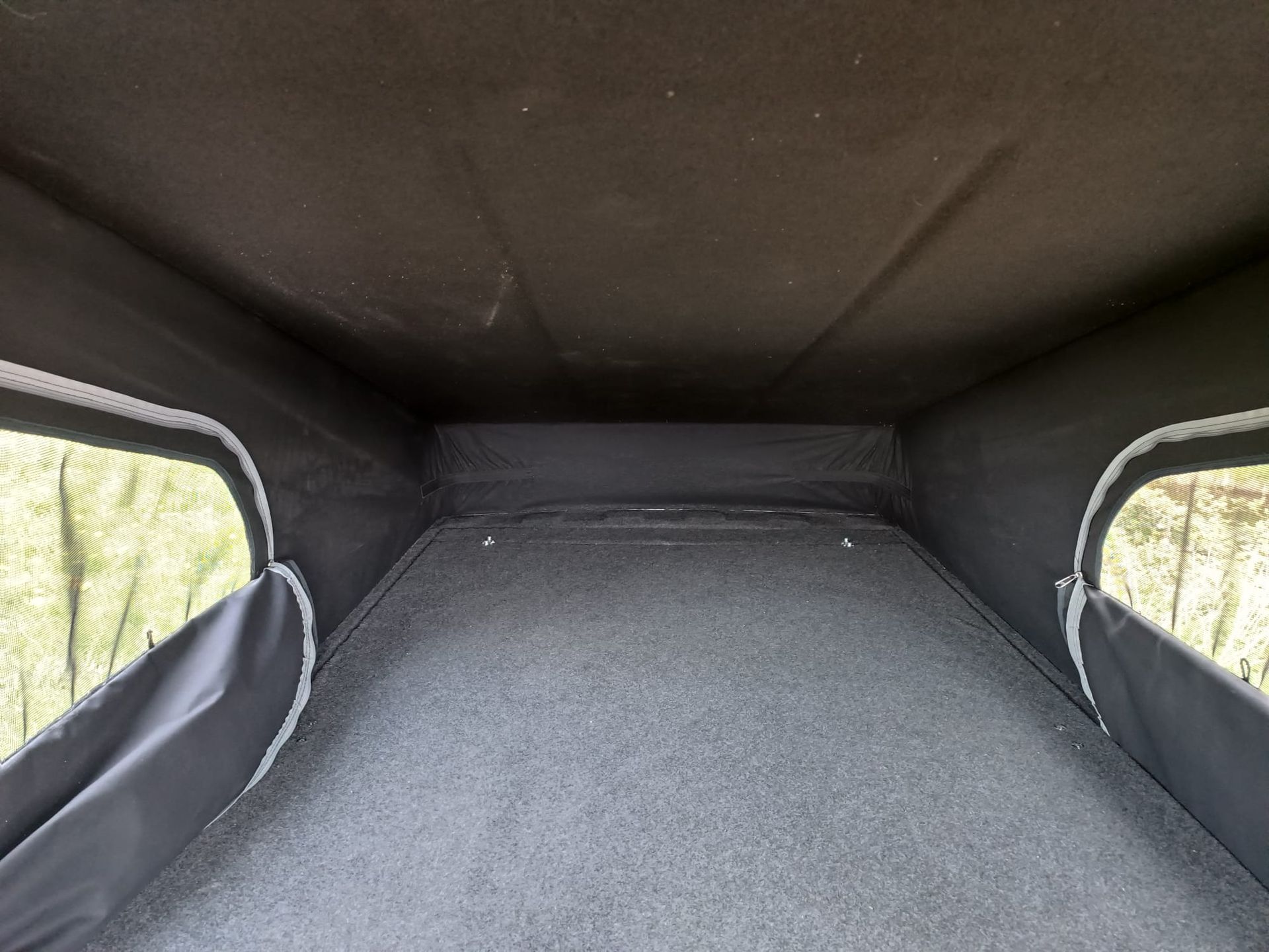 Binnenin een camperopbouw, met een donkergrijs interieur, een vloerbedekking en ramen aan beide zijden.