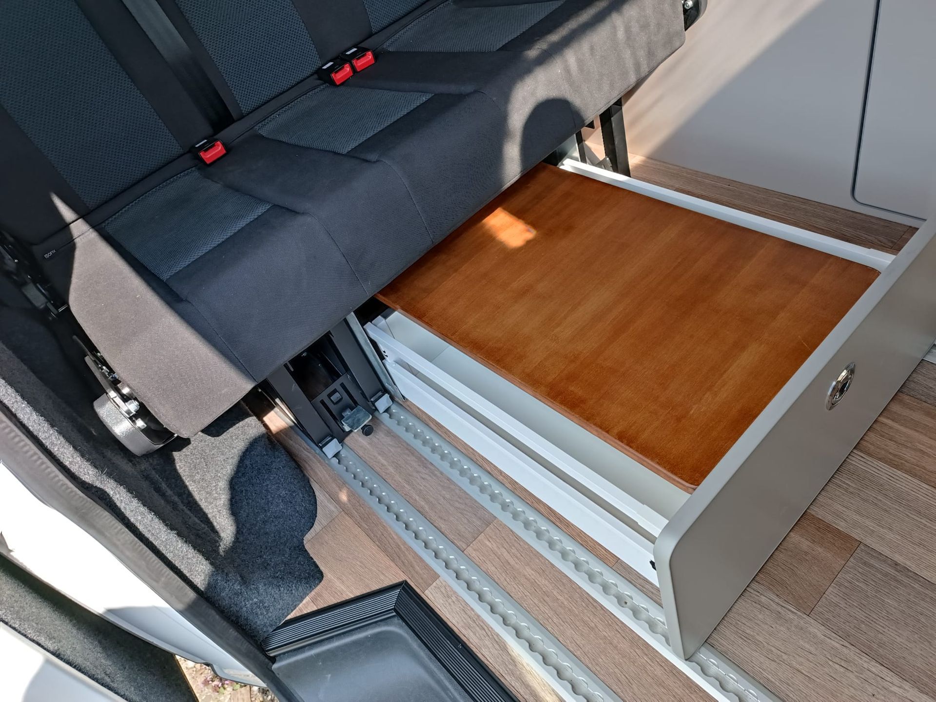 Een lade in een bestelwagen wordt geopend en onthult een houten oppervlak. Grijze kastjes staan ​​naast een zwarte bank.