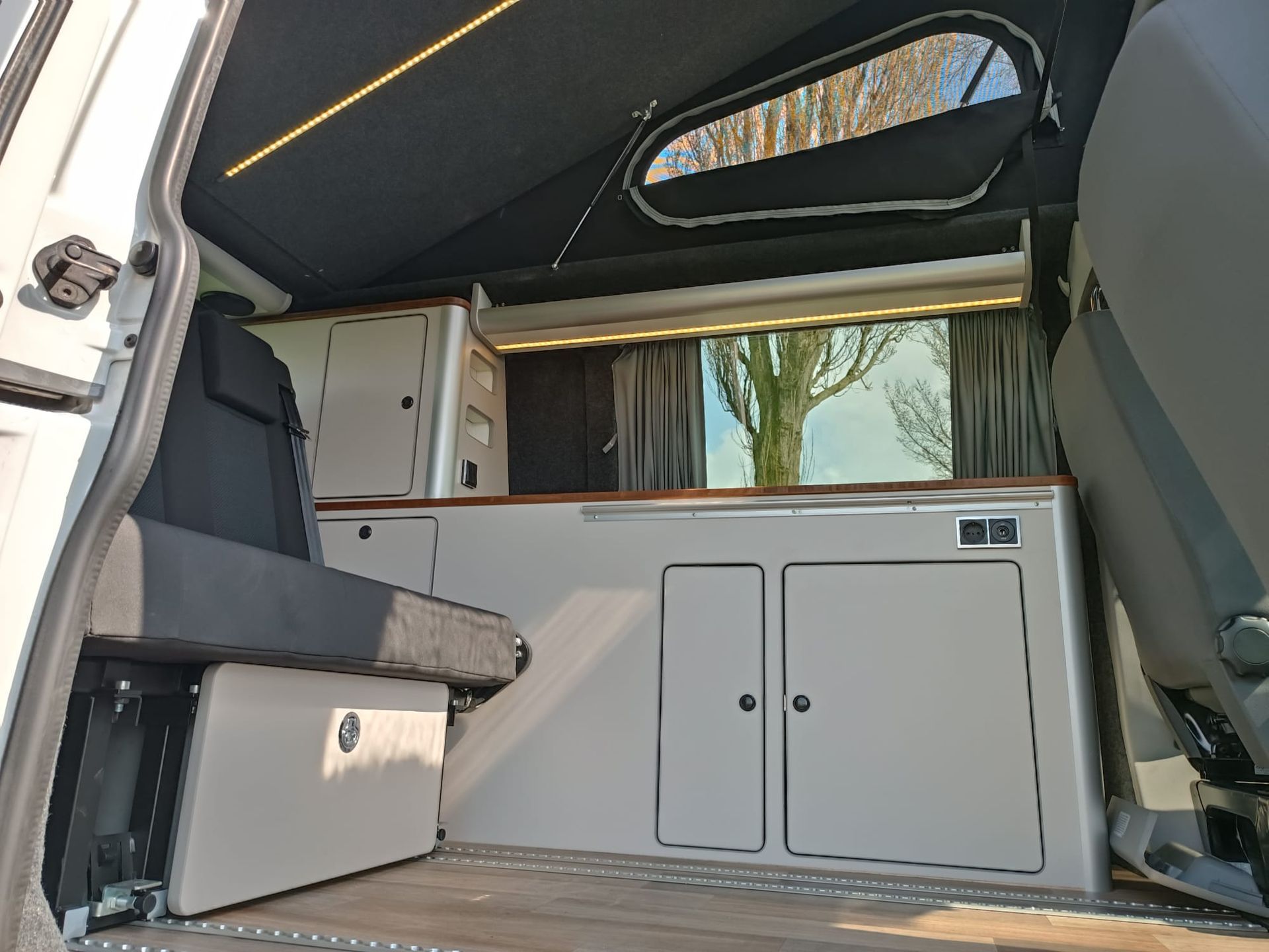 Binnenin een camper: ingebouwde kasten, zitplaatsen en een raam met uitzicht.