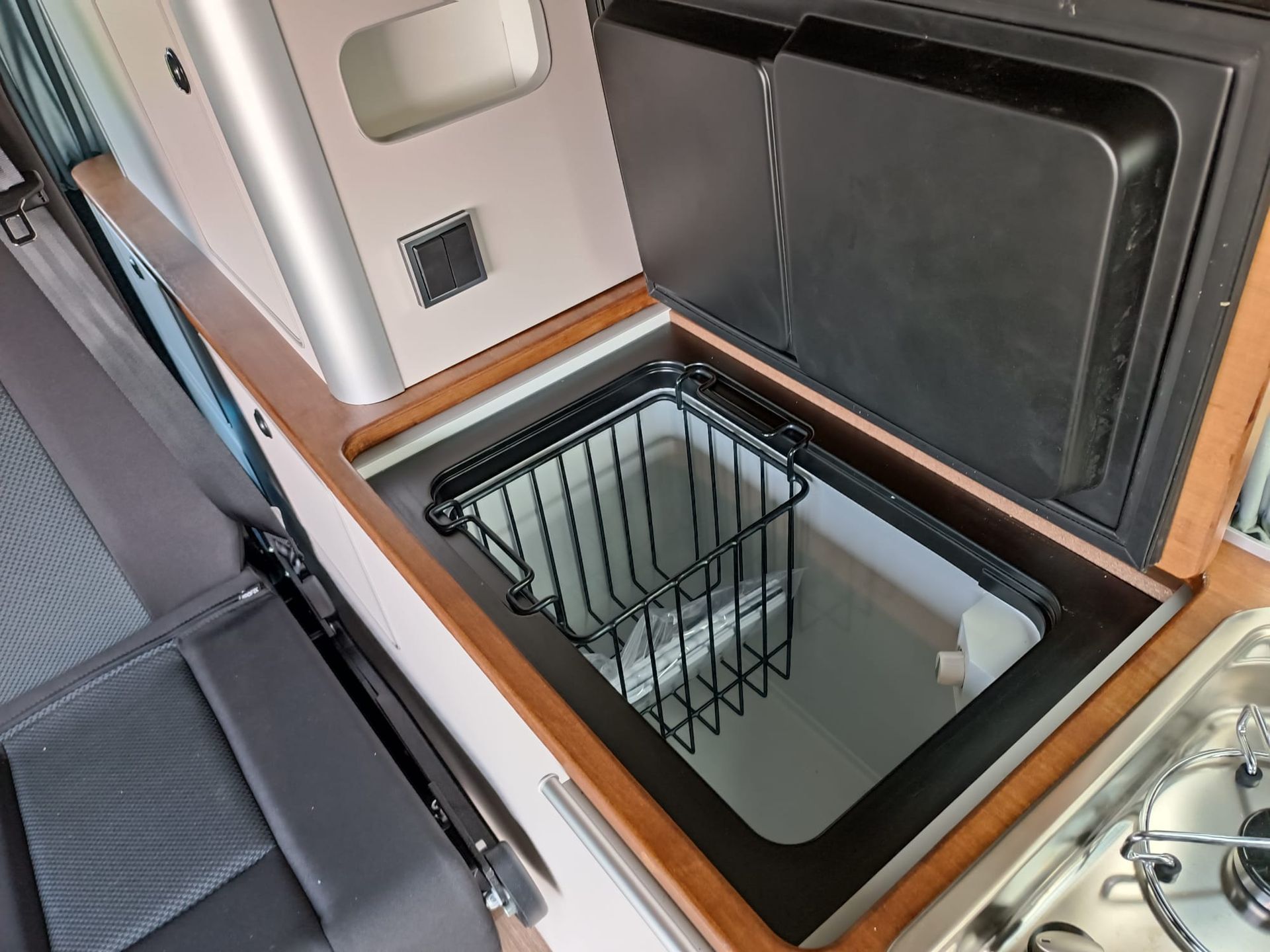 Open camperkoelkast met een metalen draadmandje erin.