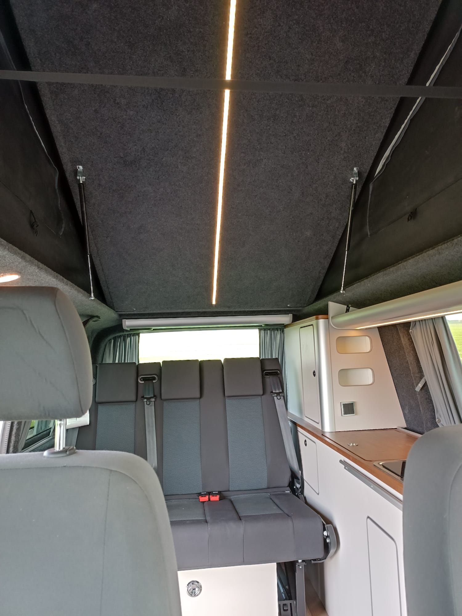 Interieur van een camperbusje met grijze stoelen en een hefdak. LED-verlichting verlicht het plafond.