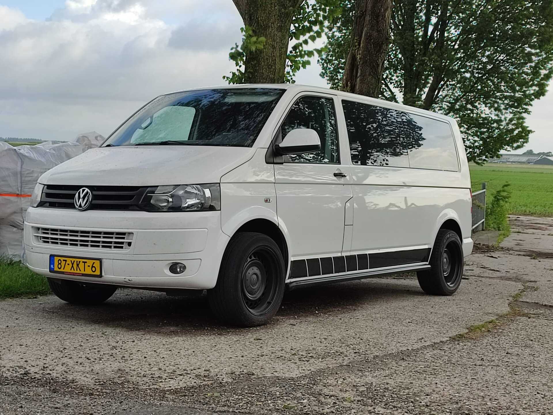 Witte Volkswagenbus geparkeerd buiten, Nederlands kenteken. Zwarte banden, zijstreep.