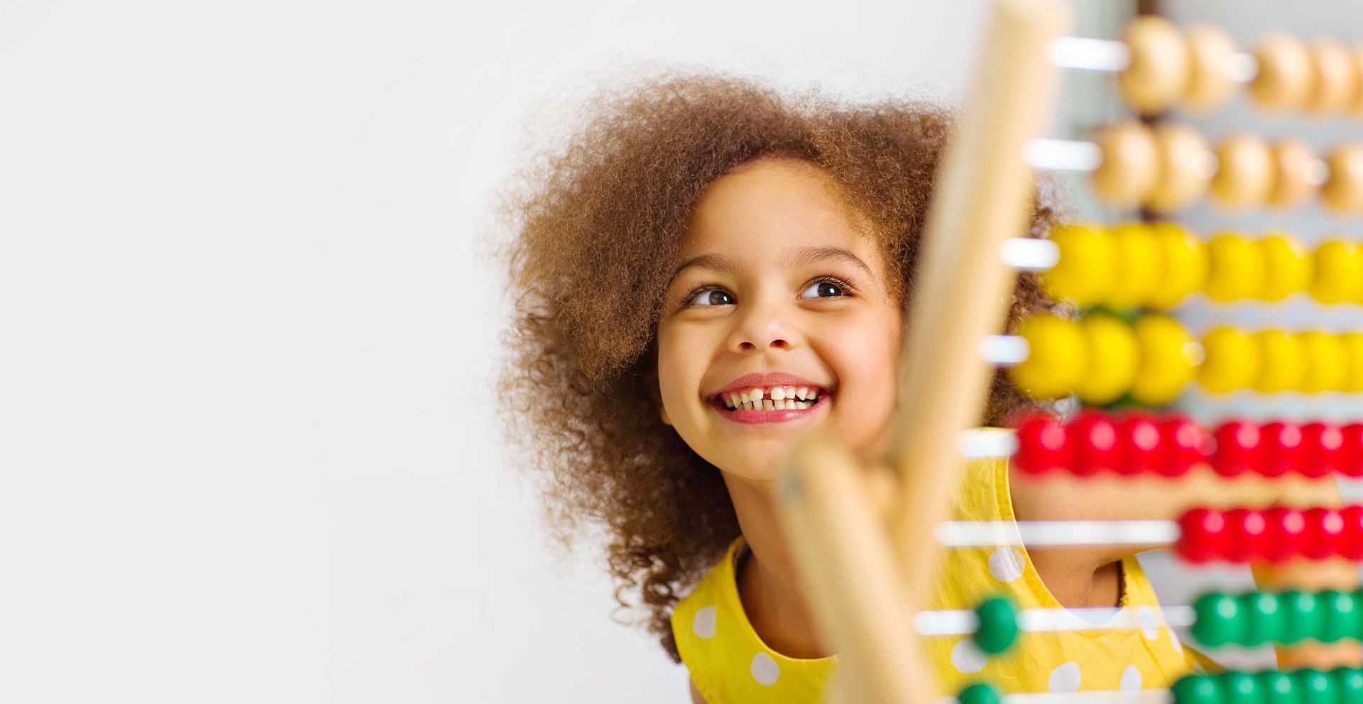 Girl with curly hair smiles while using a colorful abacus.