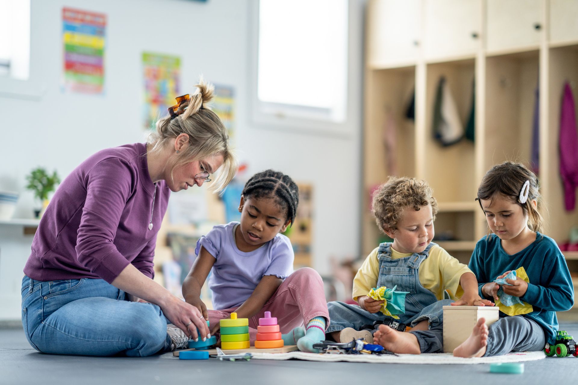 Teacher and three children playing with toys in a brightly lit classroom. Teacher and three children playing with toys in a brightly lit classroom.