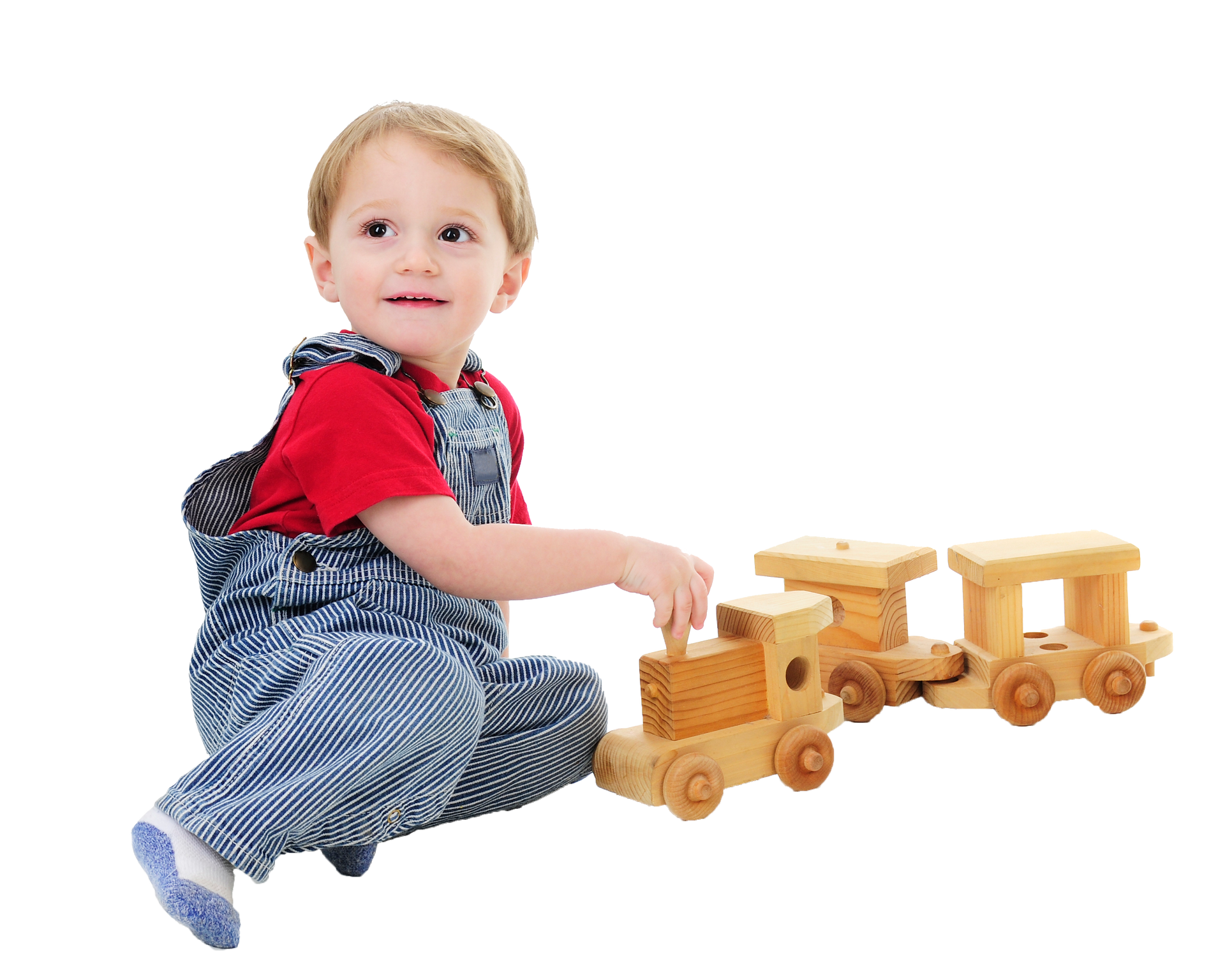 Child in overalls playing with a wooden toy train, smiling, white background.