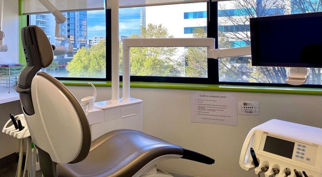 Dental office interior with chair, light, tools, and a window view of buildings.