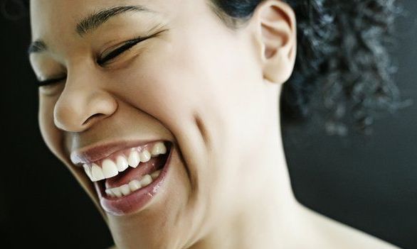 Woman with dark skin laughing with closed eyes, dimples, and a wide smile.