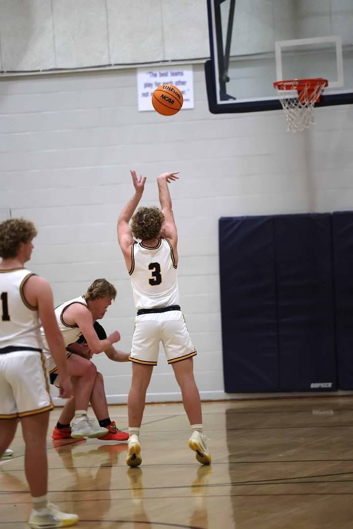 Basketball shot over defenders in a gym, with the ball near the hoop.