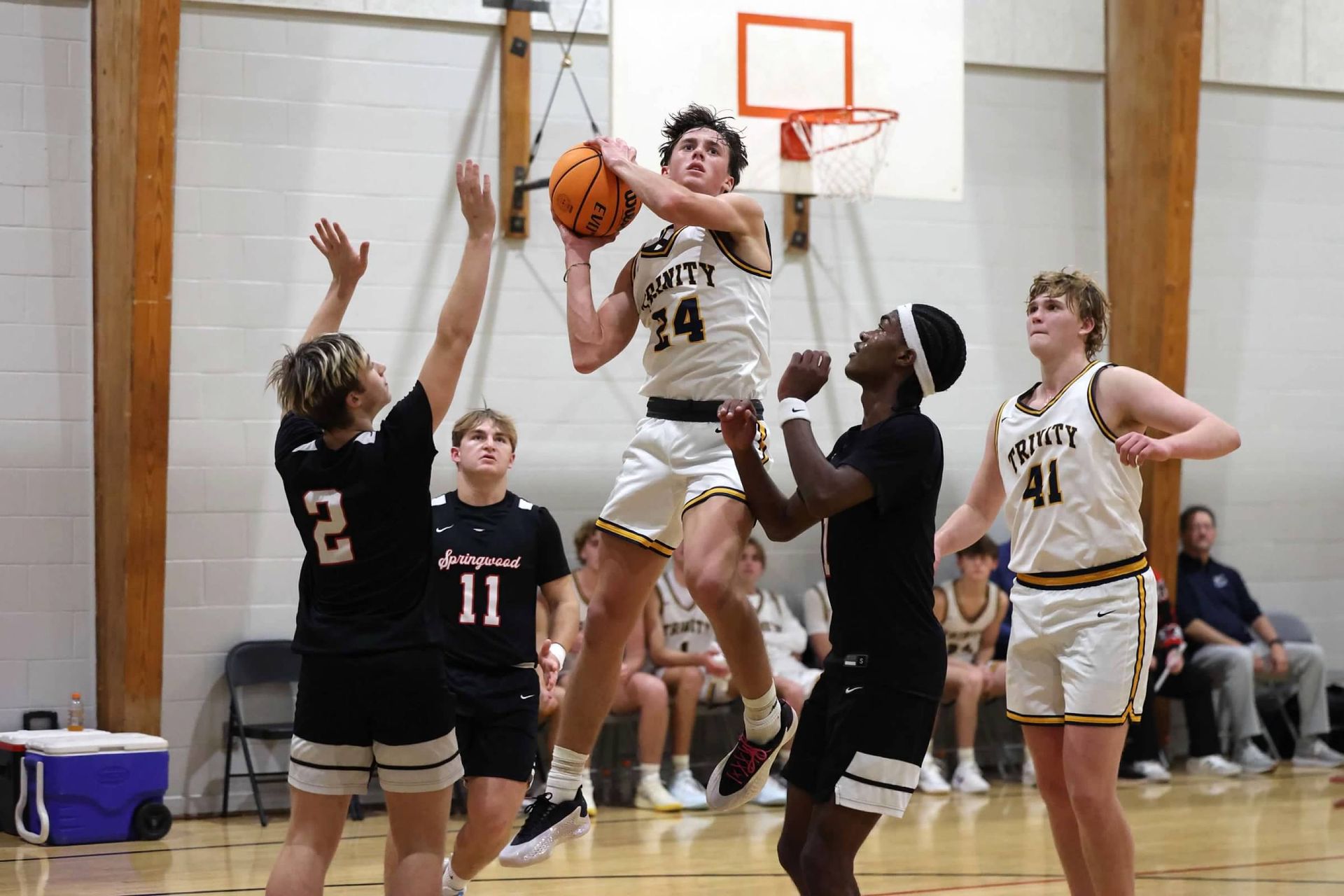 Basketball player jumps for a shot as defenders reach up near the hoop in a gym