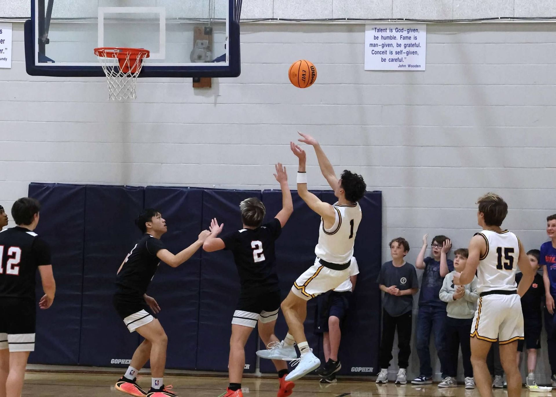 Basketball game action under the hoop, players reaching for a loose ball near the basket.