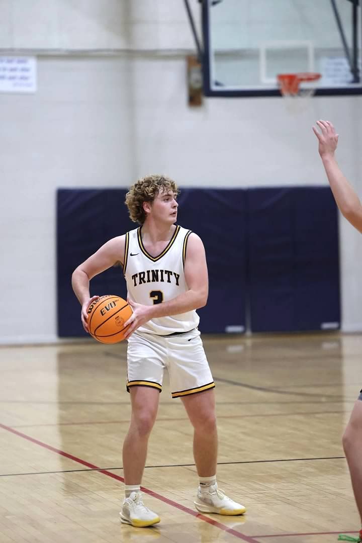 Basketball player in white jersey dribbles on an indoor court, with a hoop and defender nearby.