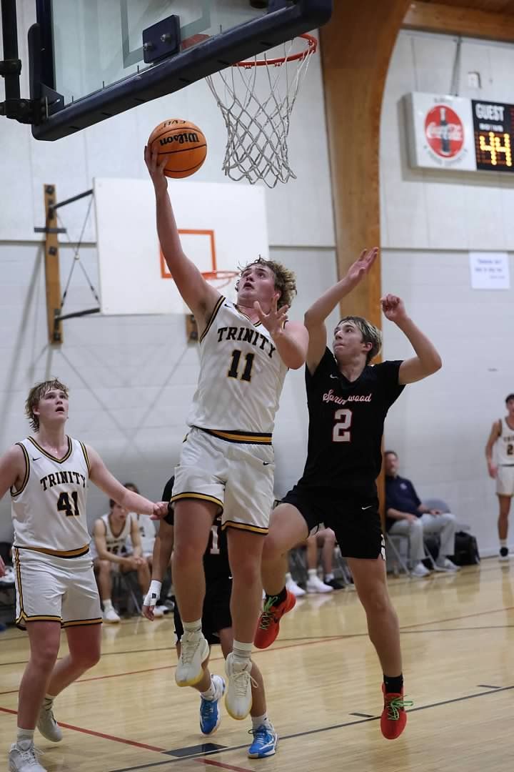 Basketball player in white leaps for a layup as defenders in black contest the shot indoors
