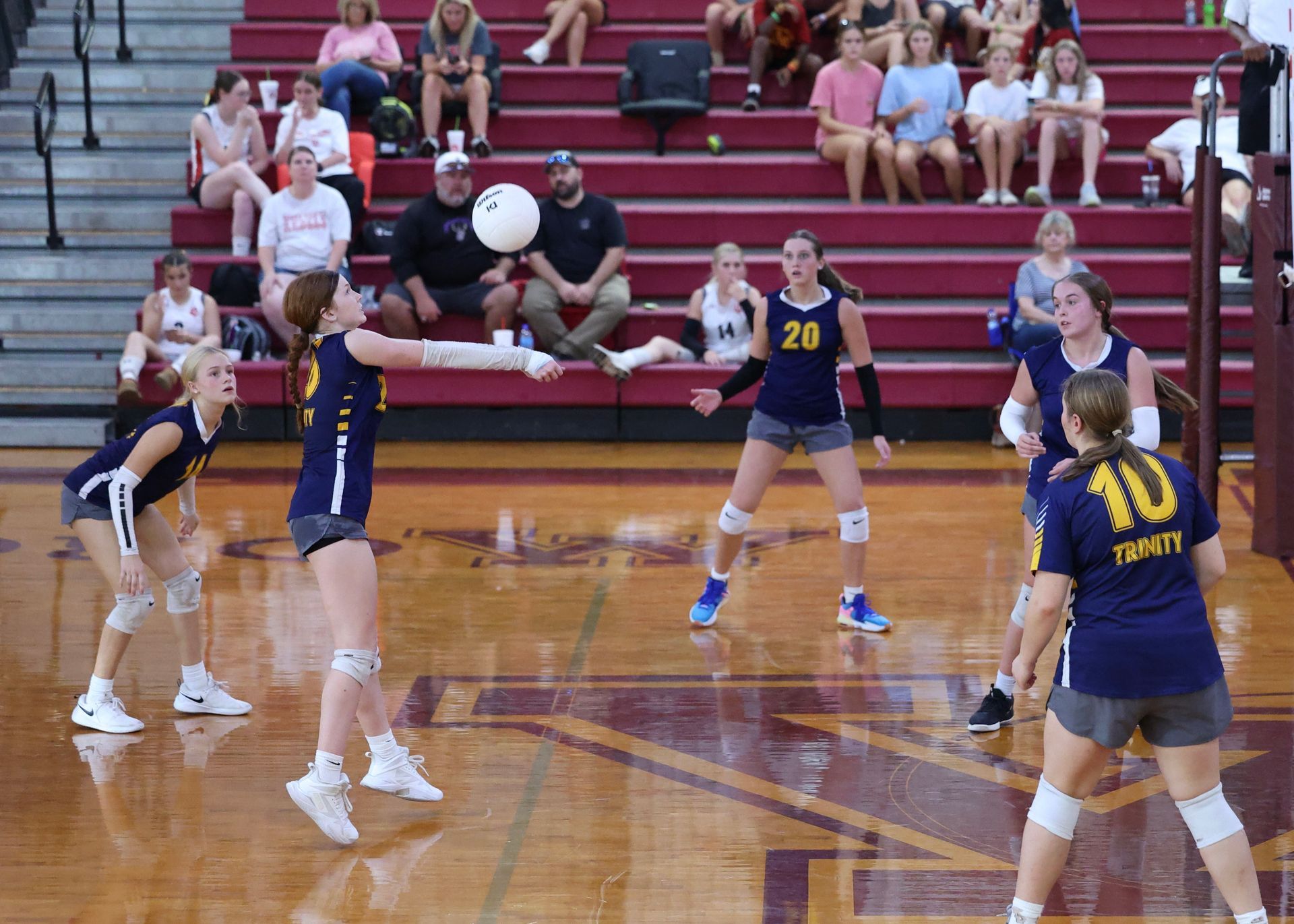 Indoor volleyball game with players in navy and white uniforms on a polished court