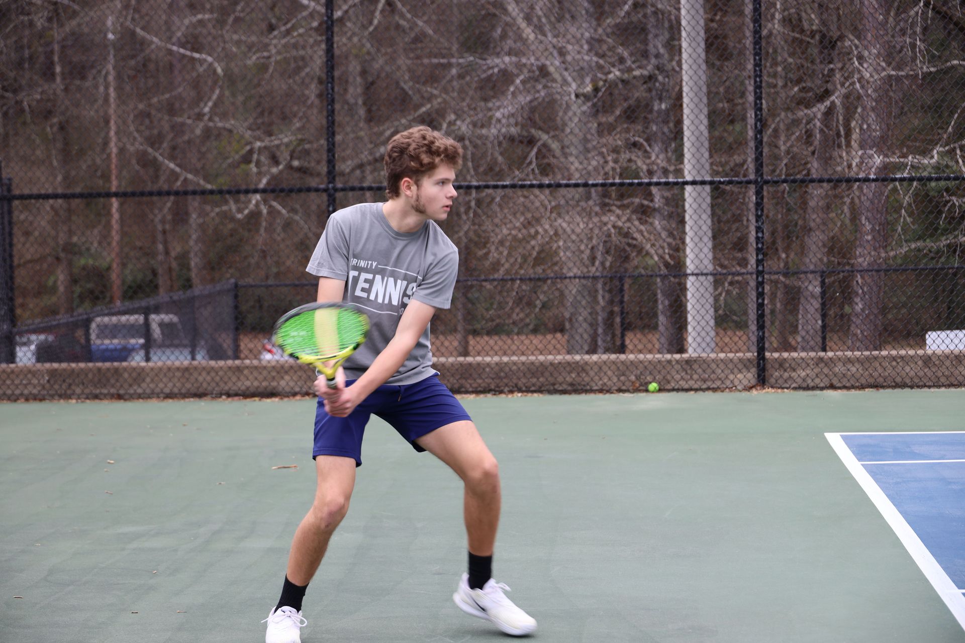 Tennis player in gray shirt and blue shorts ready to return a shot on an outdoor court