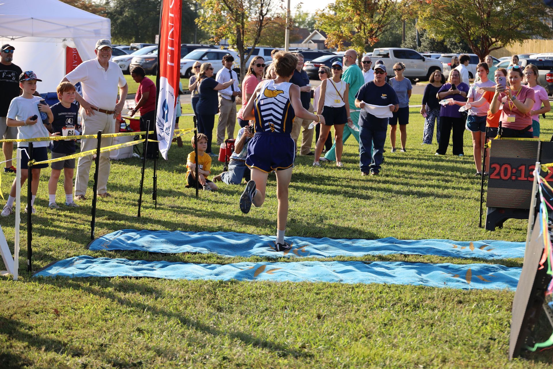 Runner finishing a race on a blue mat as spectators watch outdoors