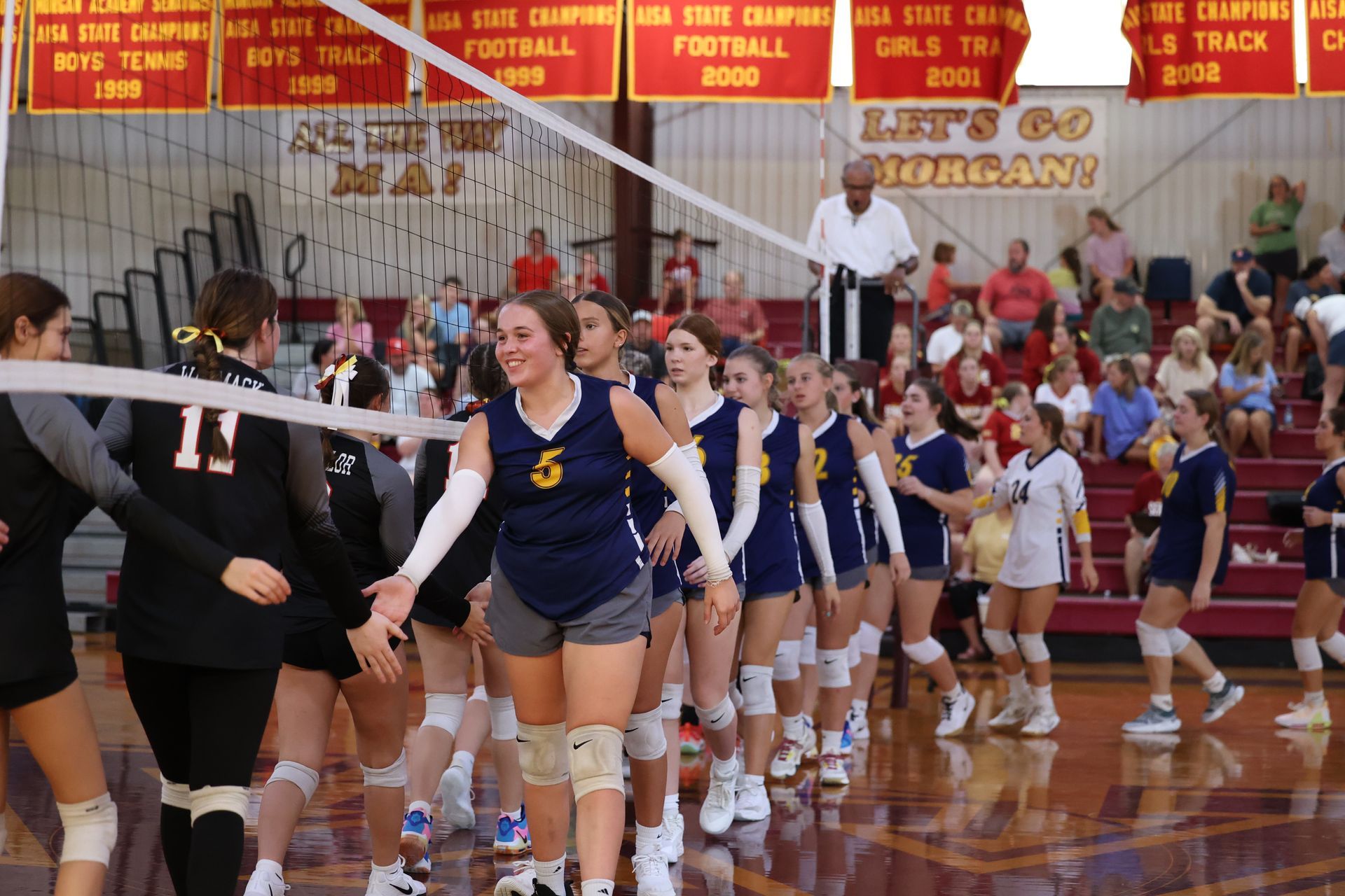 Volleyball teams lining up to shake hands on a polished indoor court after a match