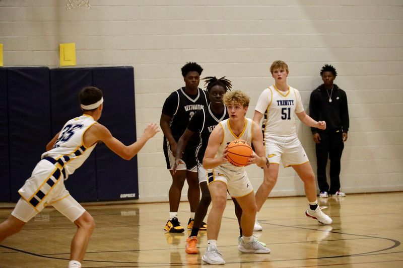 Basketball players in a gym, one dribbling while defenders close in.