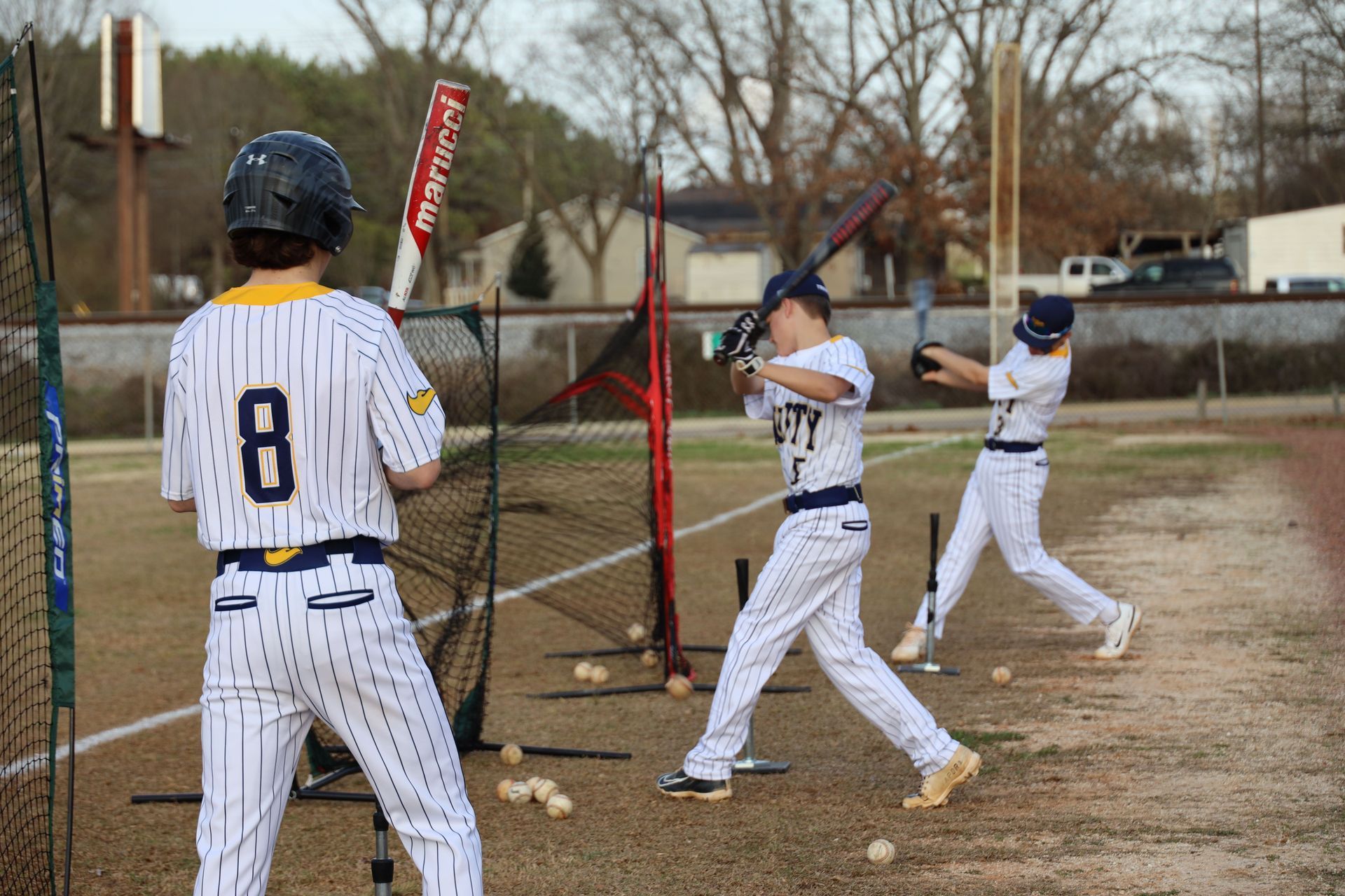 Baseball players in white uniforms warming up near a batting cage outdoors