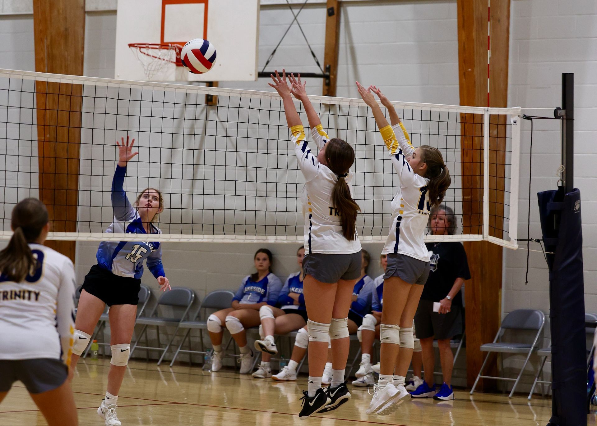 Volleyball players at the net in a gym, jumping to block a spike