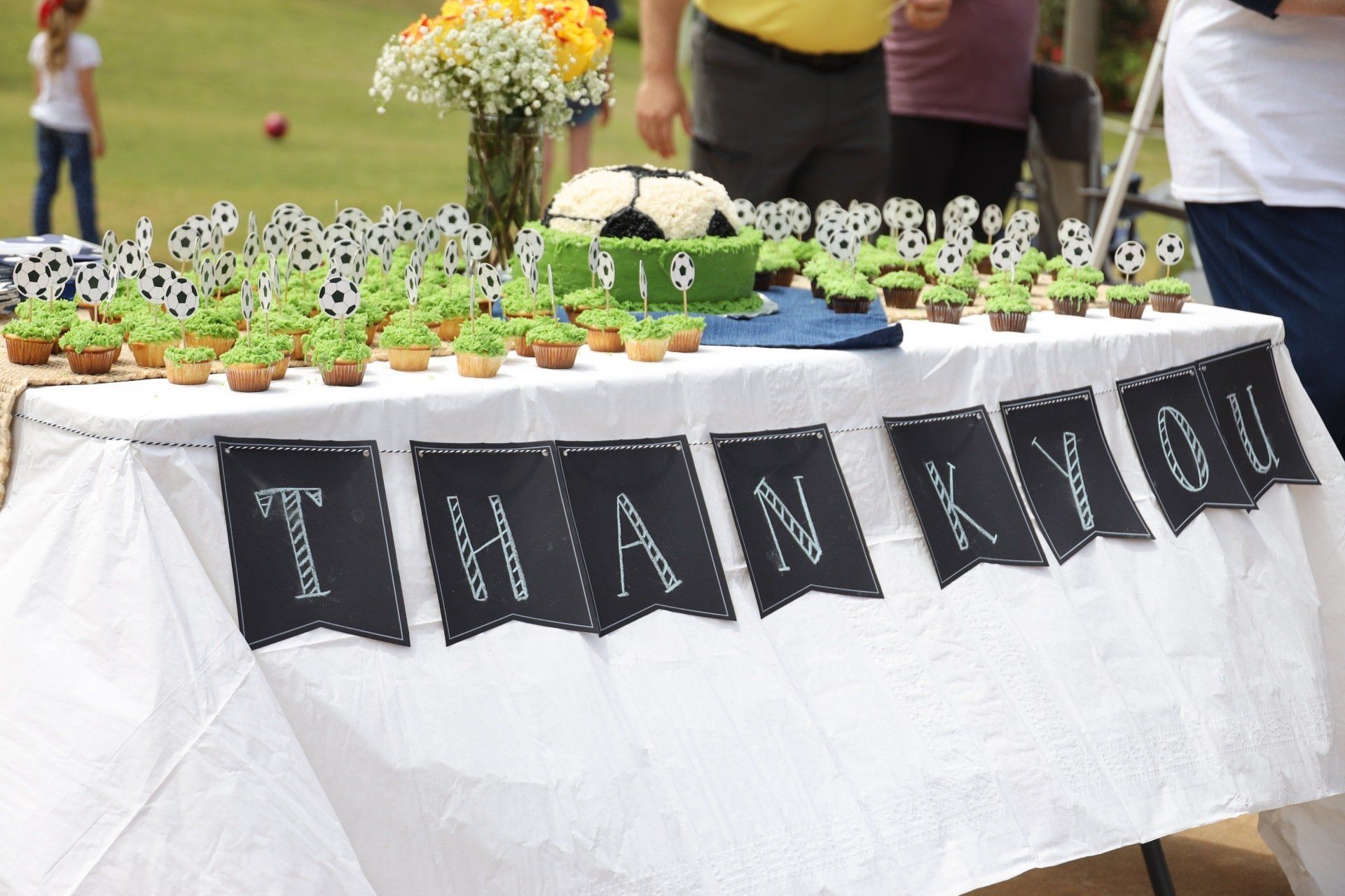 Thank-you banner on a table with flower arrangements and small plants at an outdoor event