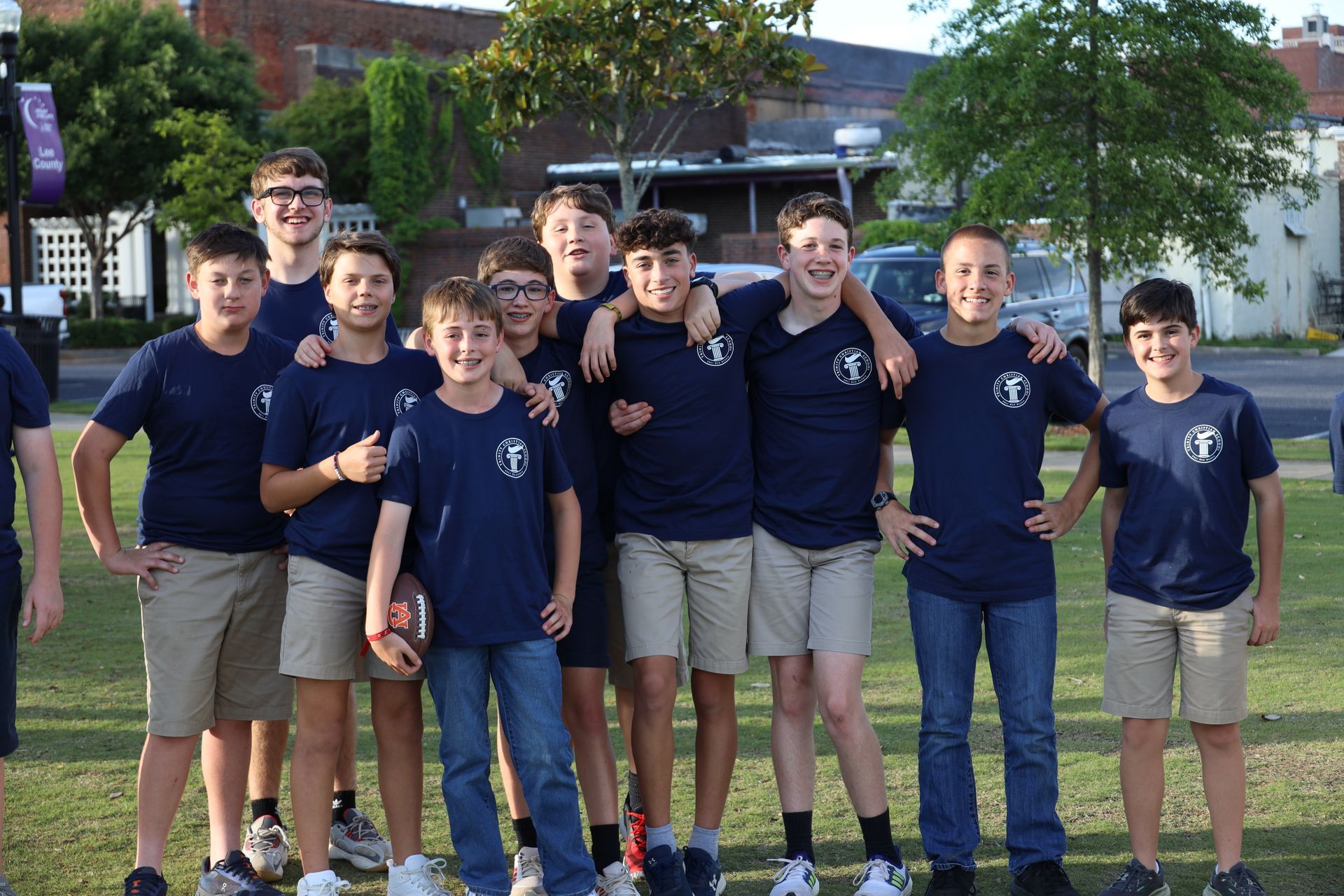 Group of students in navy shirts posing outdoors on a grassy field with a building in the background