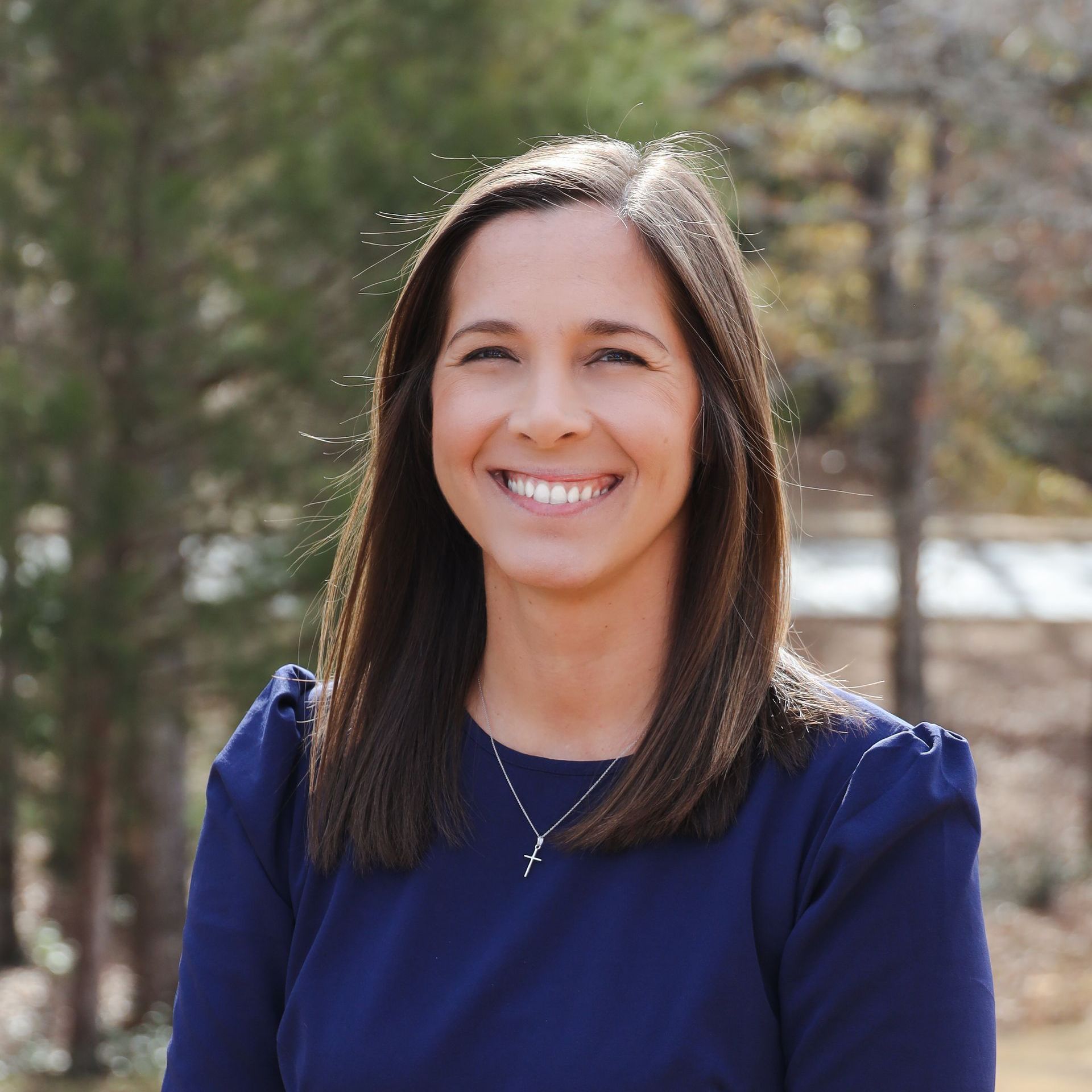 Smiling person in a navy top outdoors with trees in the background