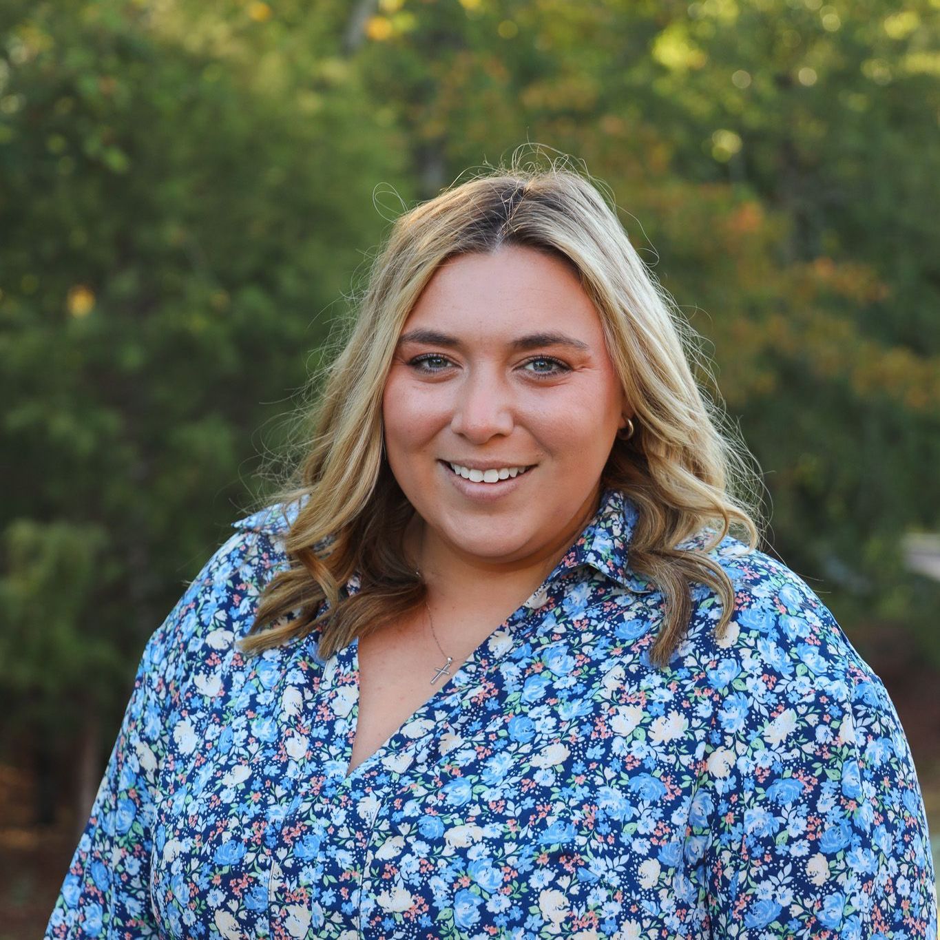 Smiling person in a blue floral shirt outdoors with a blurred green background
