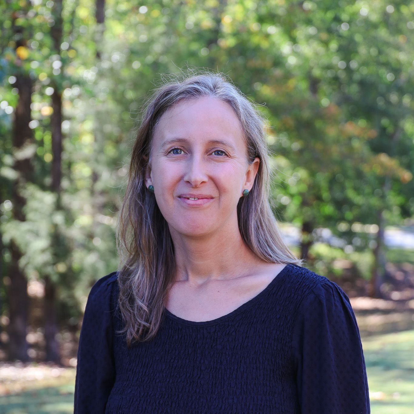 Smiling woman in a black top standing outdoors with trees in the background