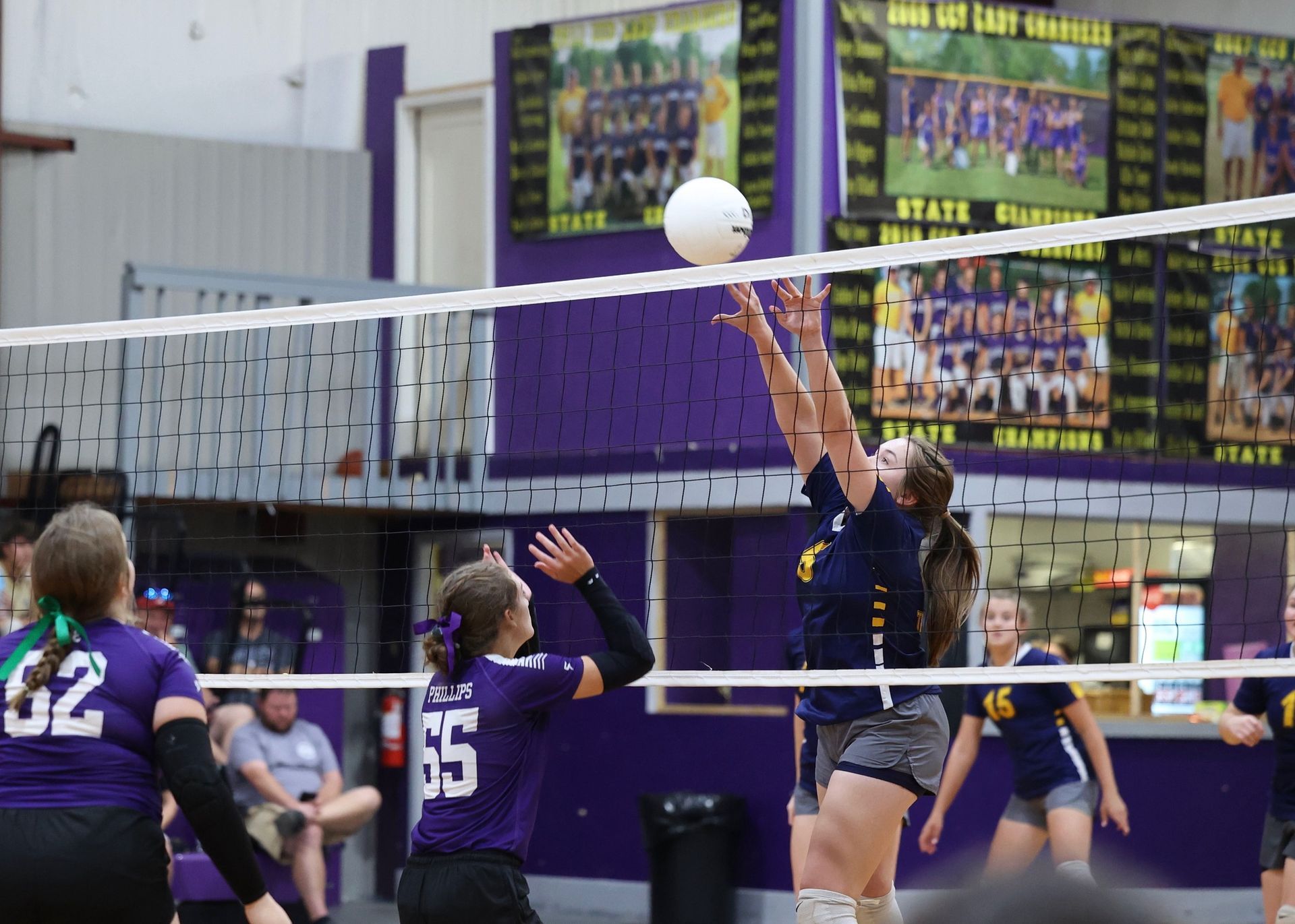 Women’s volleyball game: player in navy jumps to set the ball near the net