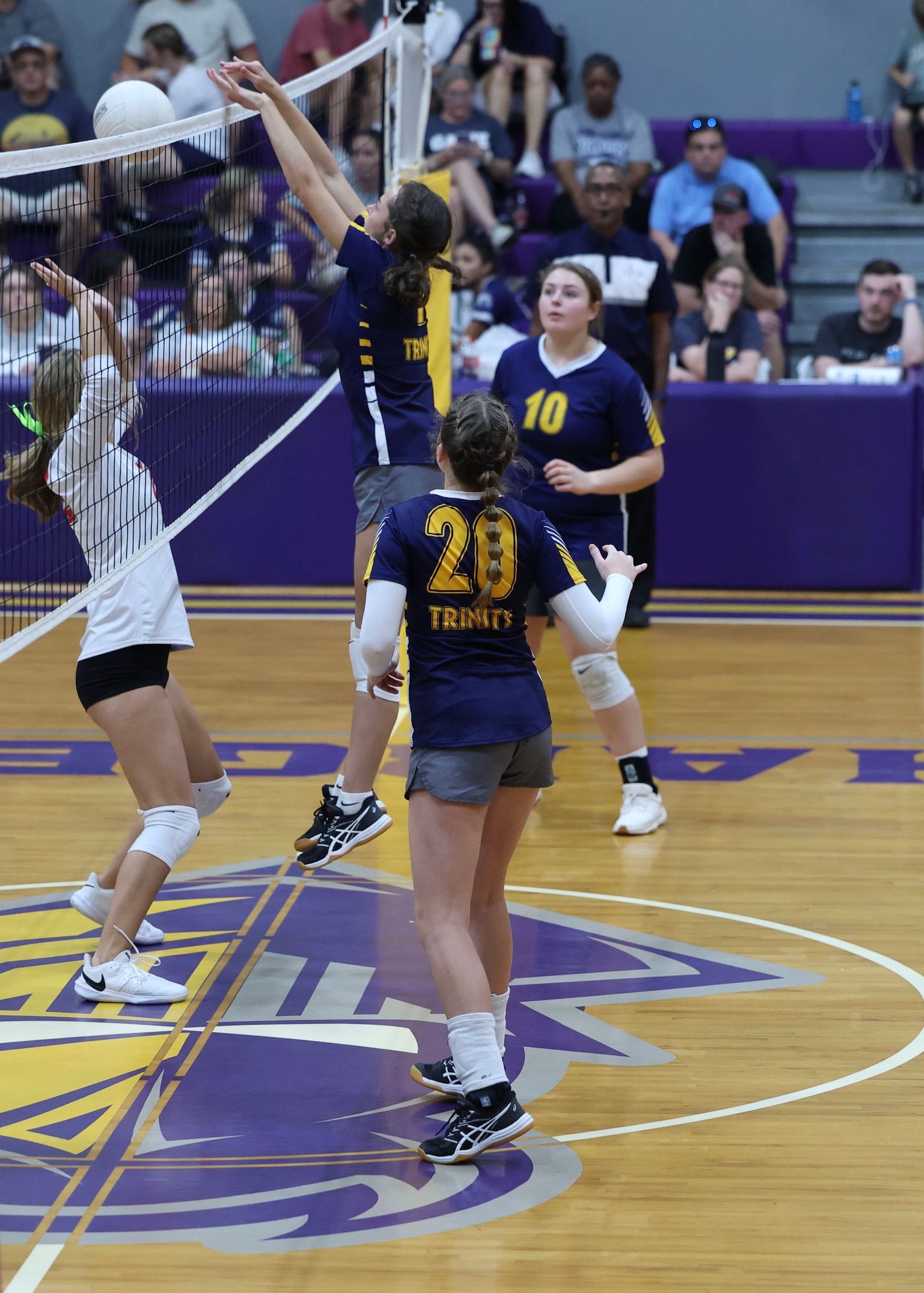 Women’s volleyball players jumping at the net during a game on a purple court