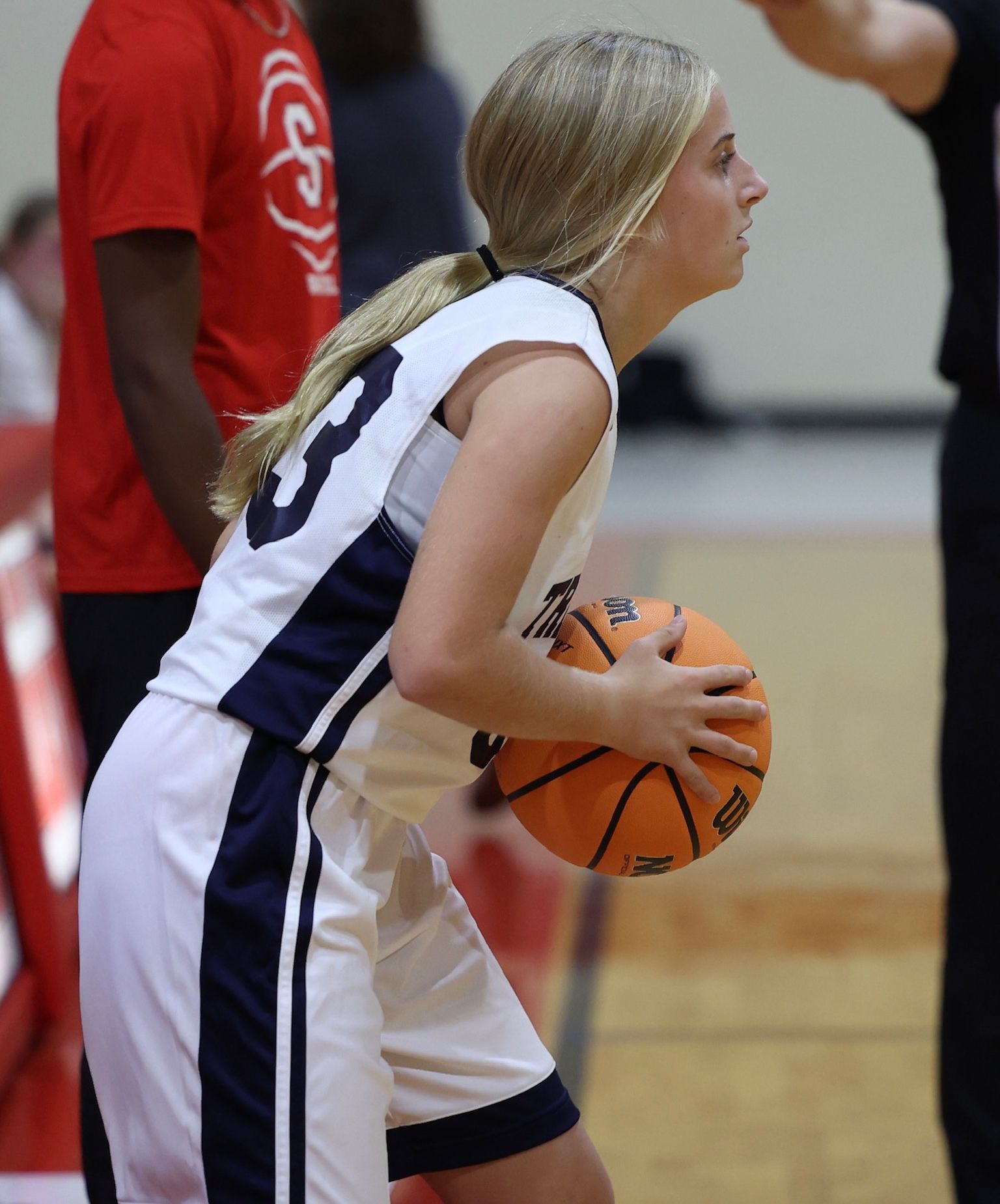 Basketball player in white and navy uniform holding the ball, preparing to pass on court