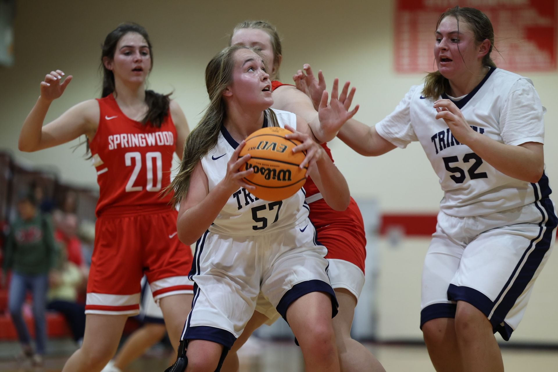 Girls' basketball game with a white player dribbling between defenders in red and white uniforms