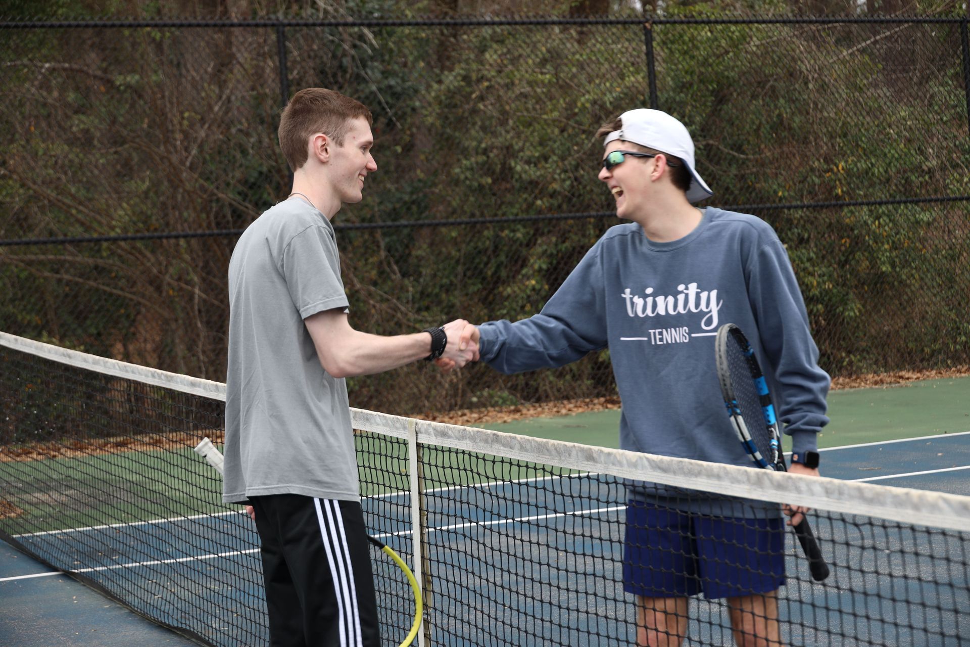 Two tennis players shake hands at the net on an outdoor court.