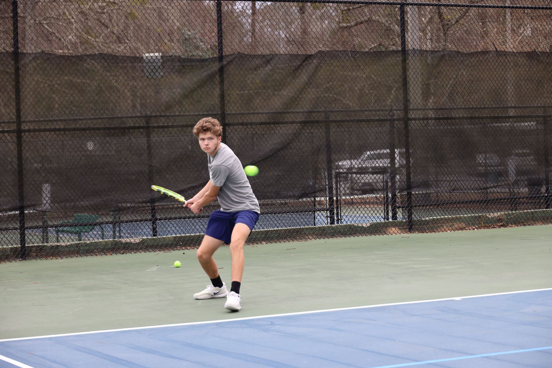 Tennis player in gray shirt prepares a backhand on an outdoor court.