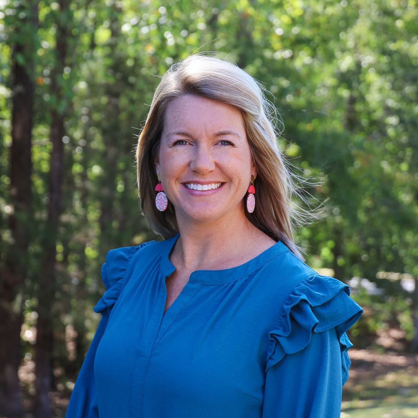Smiling woman in a blue blouse standing outdoors in a wooded area