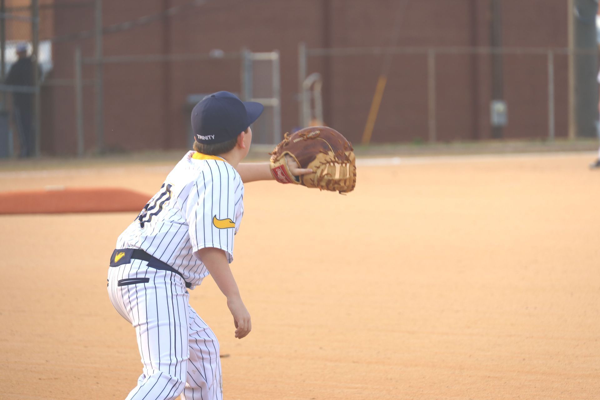 Youth baseball player in white pinstripes and navy cap fielding a ground ball on a dusty infield
