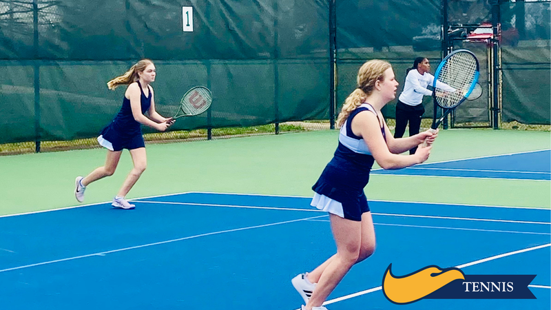 Tennis players practicing on an outdoor court, with one player serving and others ready to return.