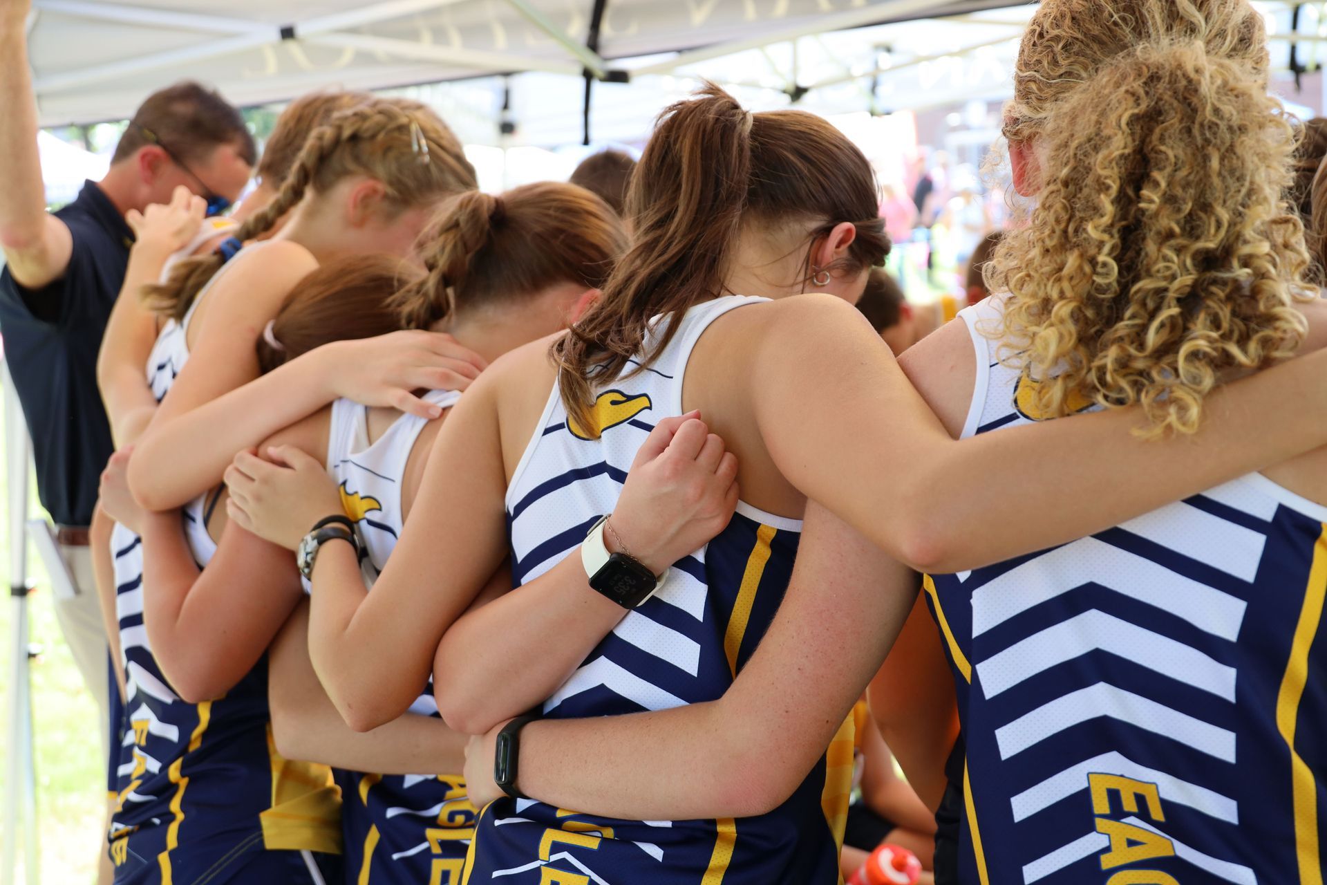 Row of athletes in navy-and-white uniforms standing arm in arm under a tent
