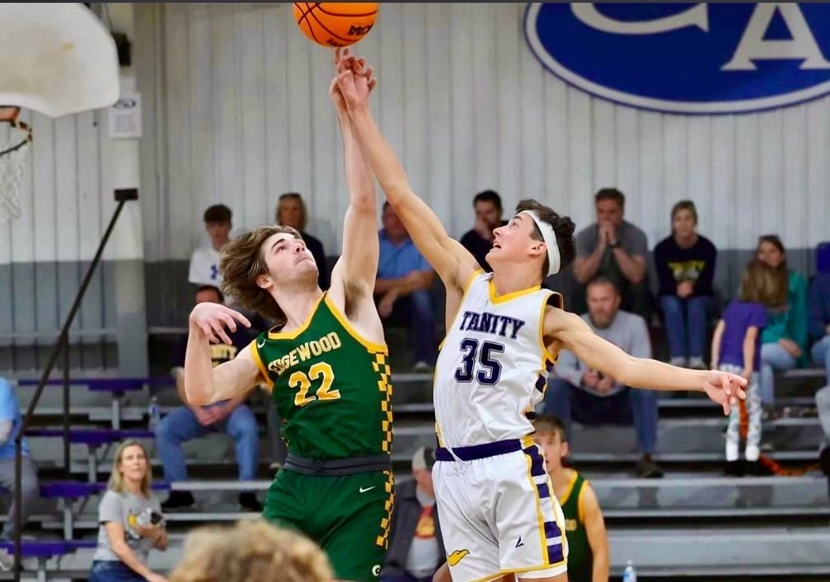 Two basketball players leap for a tip-off, one in green and one in white, under the hoop.