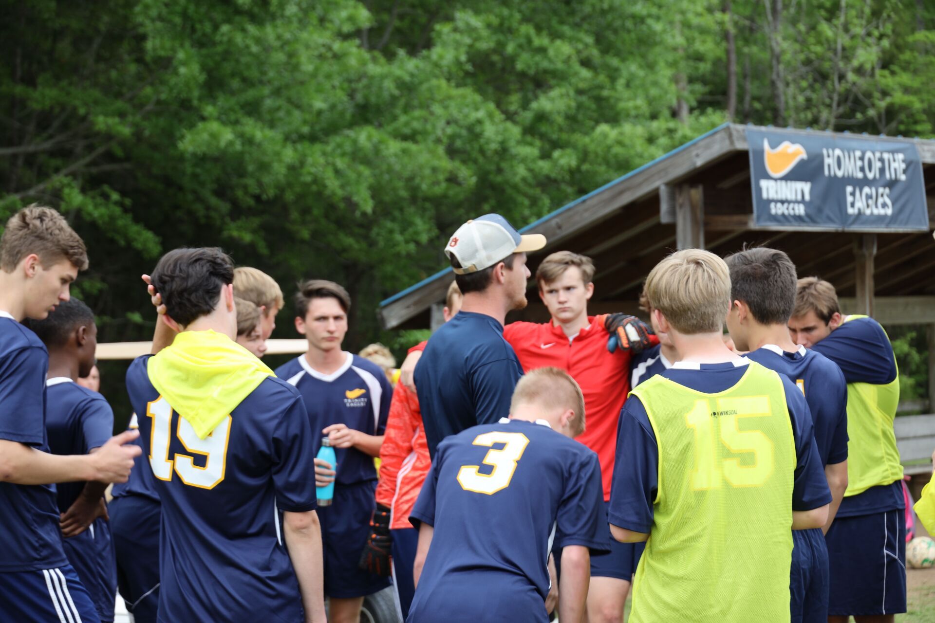 Youth soccer team huddles on a field, wearing blue and neon yellow jerseys.