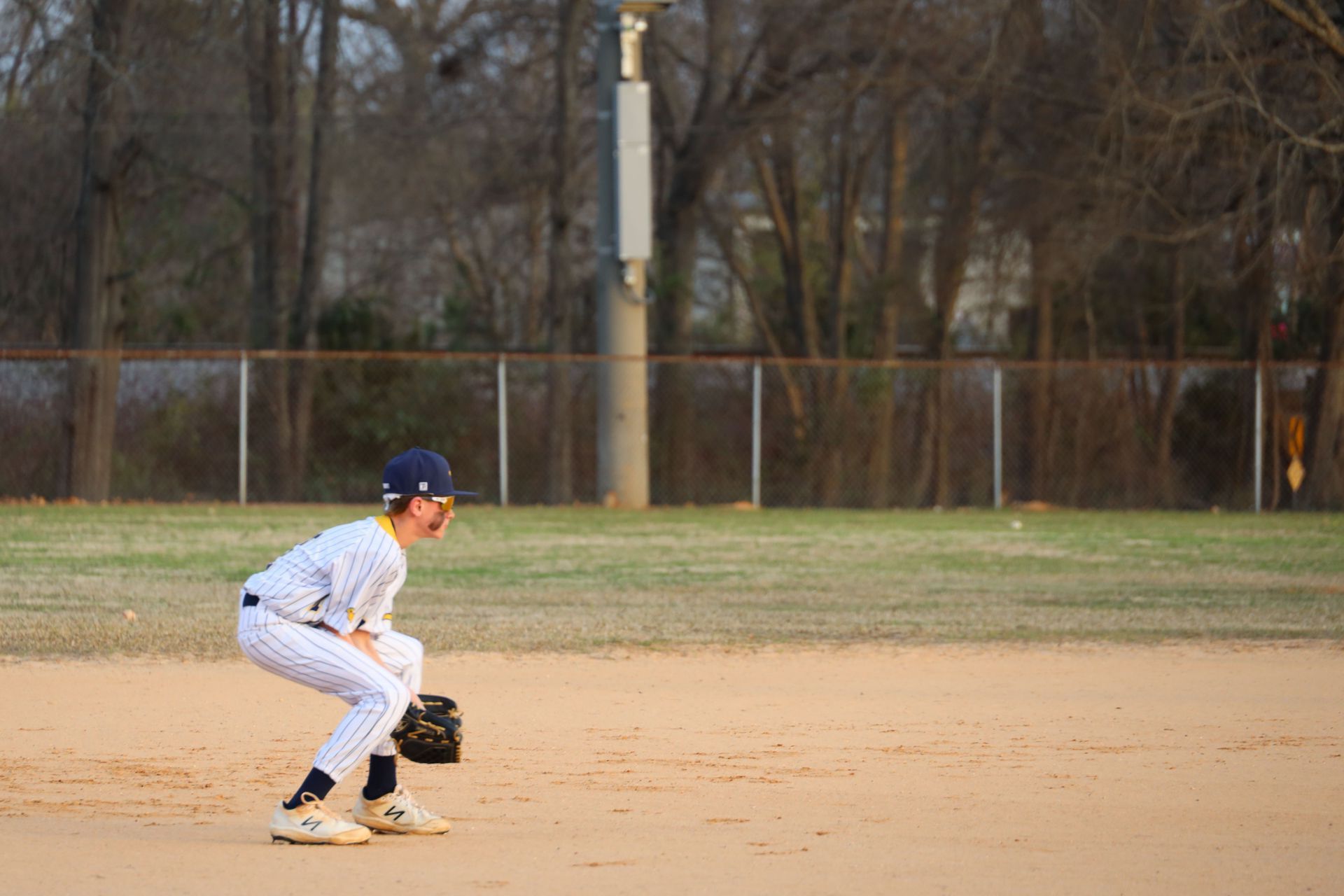 Baseball player in white uniform crouches on the infield, ready to field a ground ball.